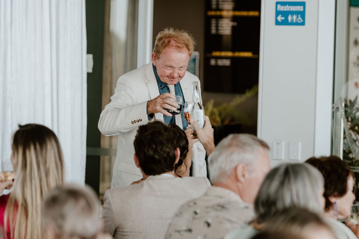 A person delivers an animated toast speech to wedding guests while standing and holding a microphone.