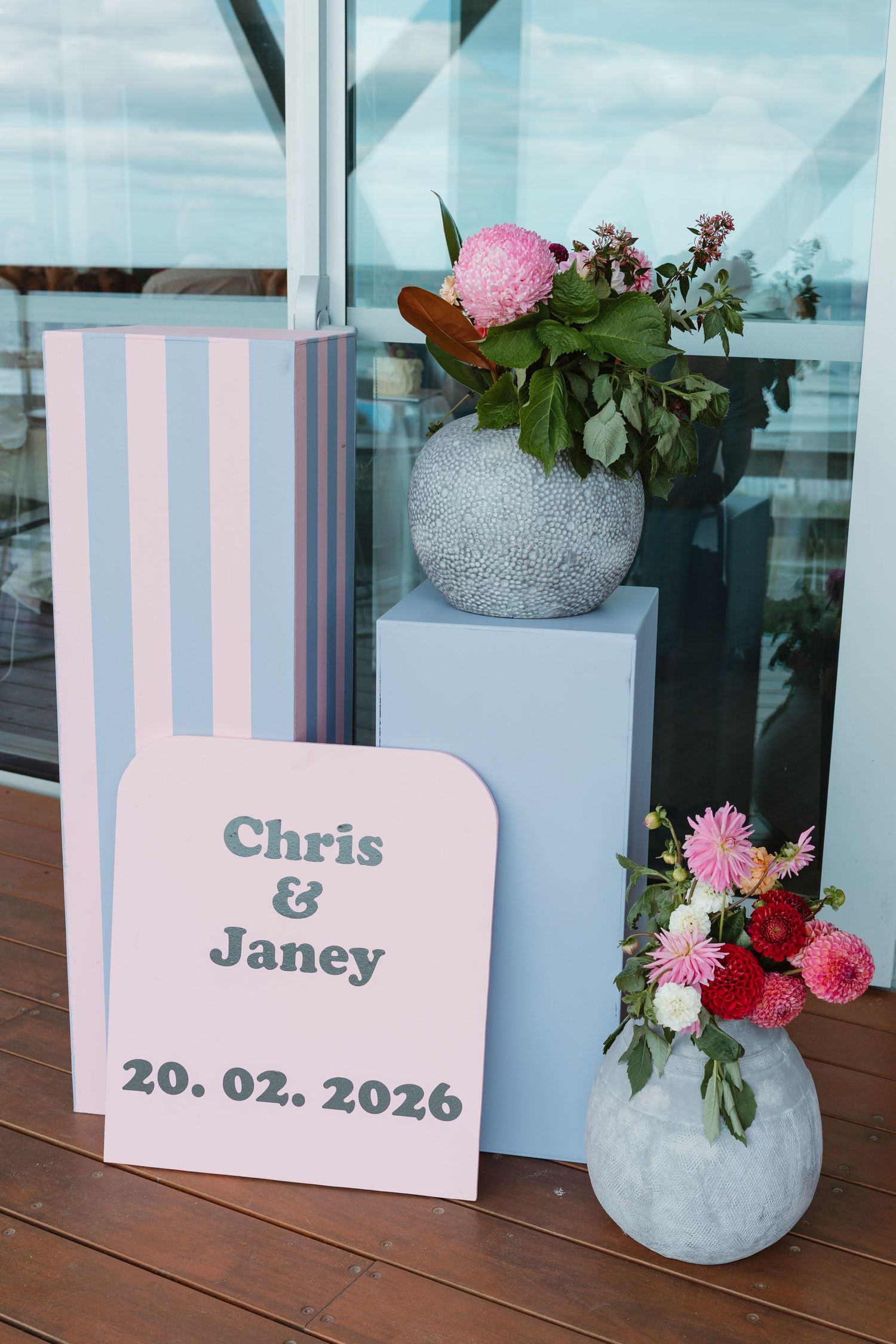Wedding welcome sign for Chris and Janey dated 20.02.2026 with pink stripe backdrop and floral arrangements in stone vases.