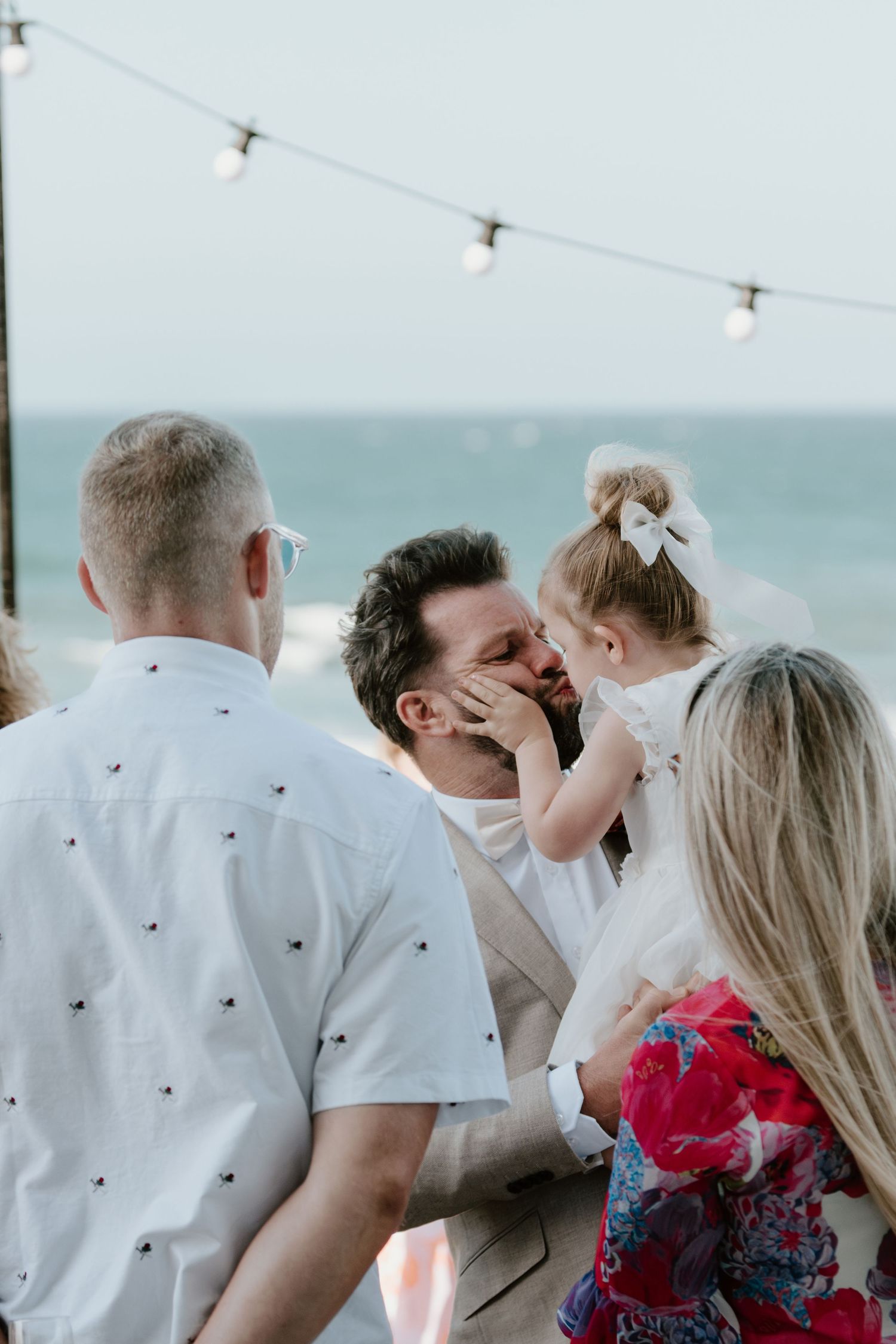 Wedding guests enjoying a casual outdoor gathering with string lights overhead. Papamoa Surf Lifesaving Club Wedding