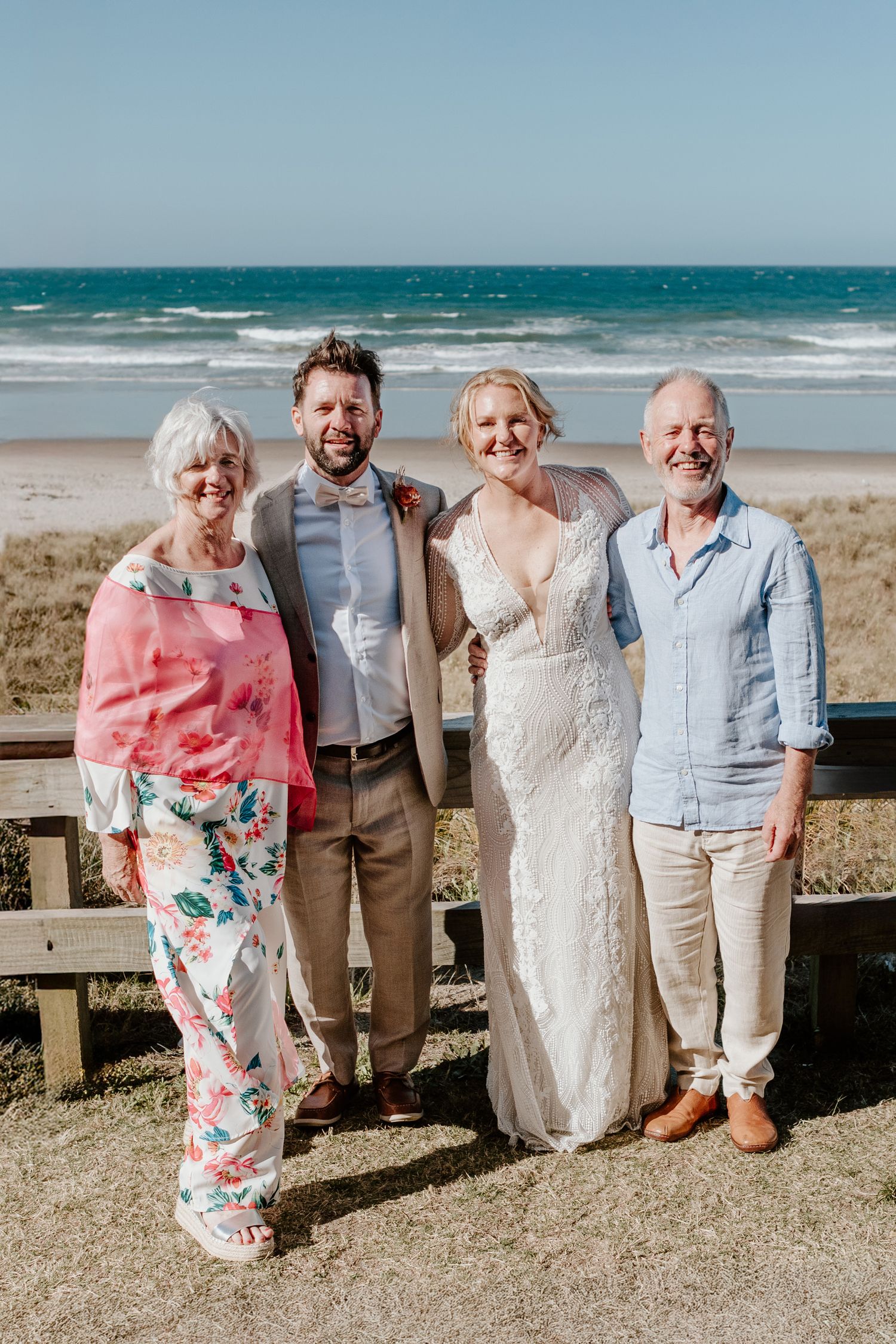 Wedding party members pose for formal photos on beach boardwalk overlooking ocean. Papamoa Surf Lifesaving Club Wedding