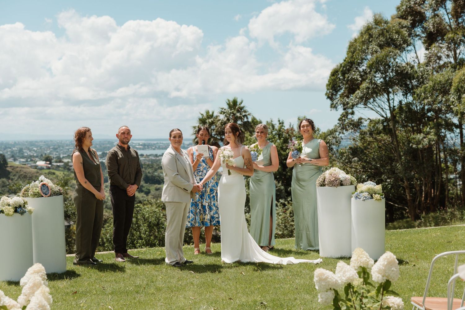 Wedding ceremony takes place on a hilltop overlooking a scenic valley with white floral arrangements and mint green decor.