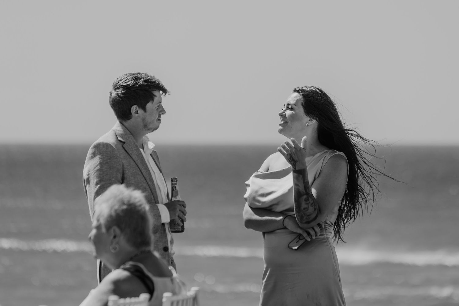 Black and white photo of a man and woman conversing on a beach with ocean waves in the background.