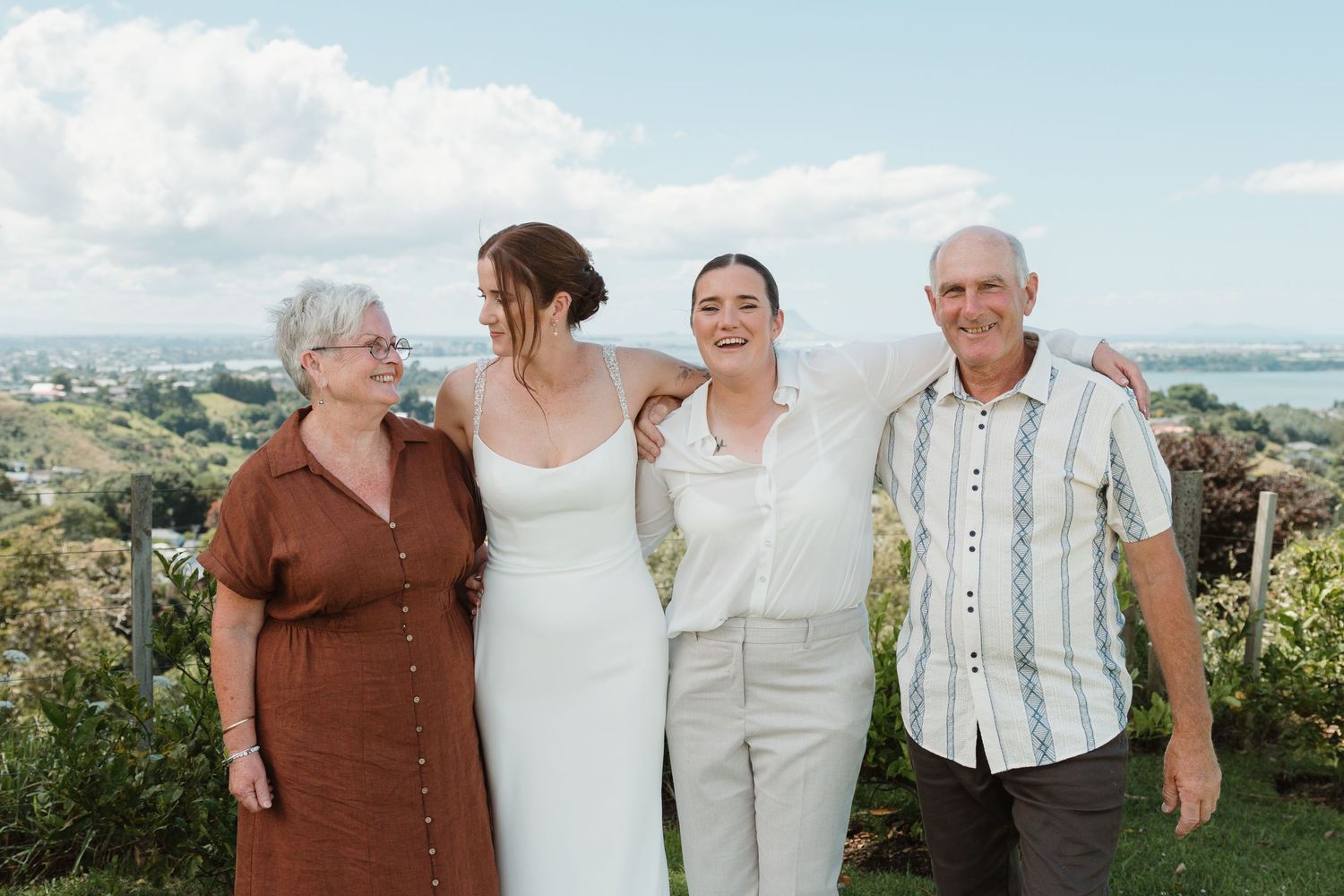 Four people smiling outdoors at a wedding celebration with scenic landscape views in the background.