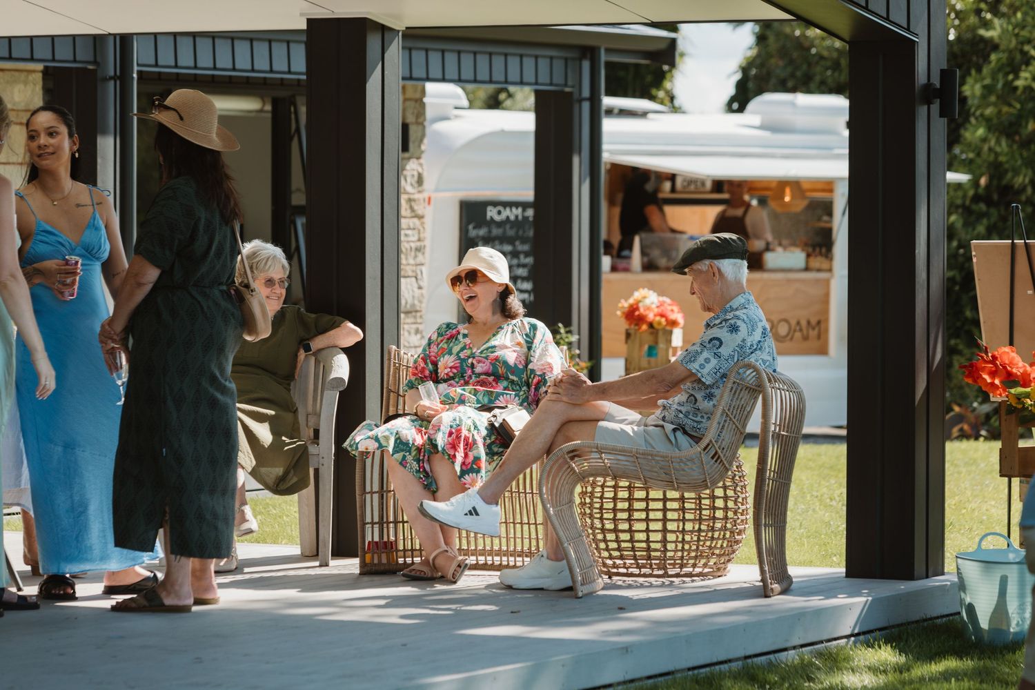 People relaxing outdoors at a stylish summer event with a food truck and lush green lawn backdrop.