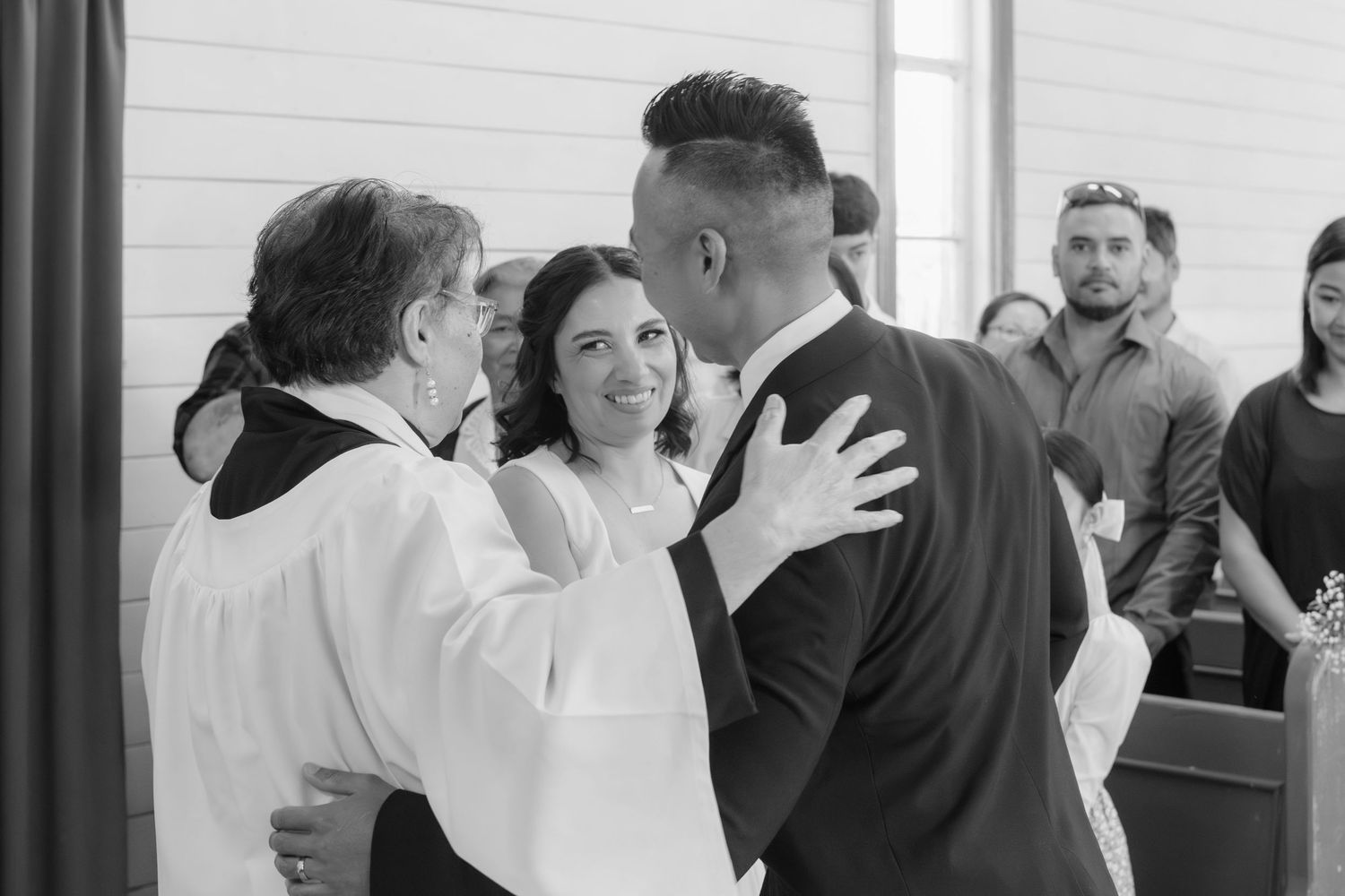 A black and white photo of a wedding ceremony with a religious official blessing a couple in a simple indoor setting.