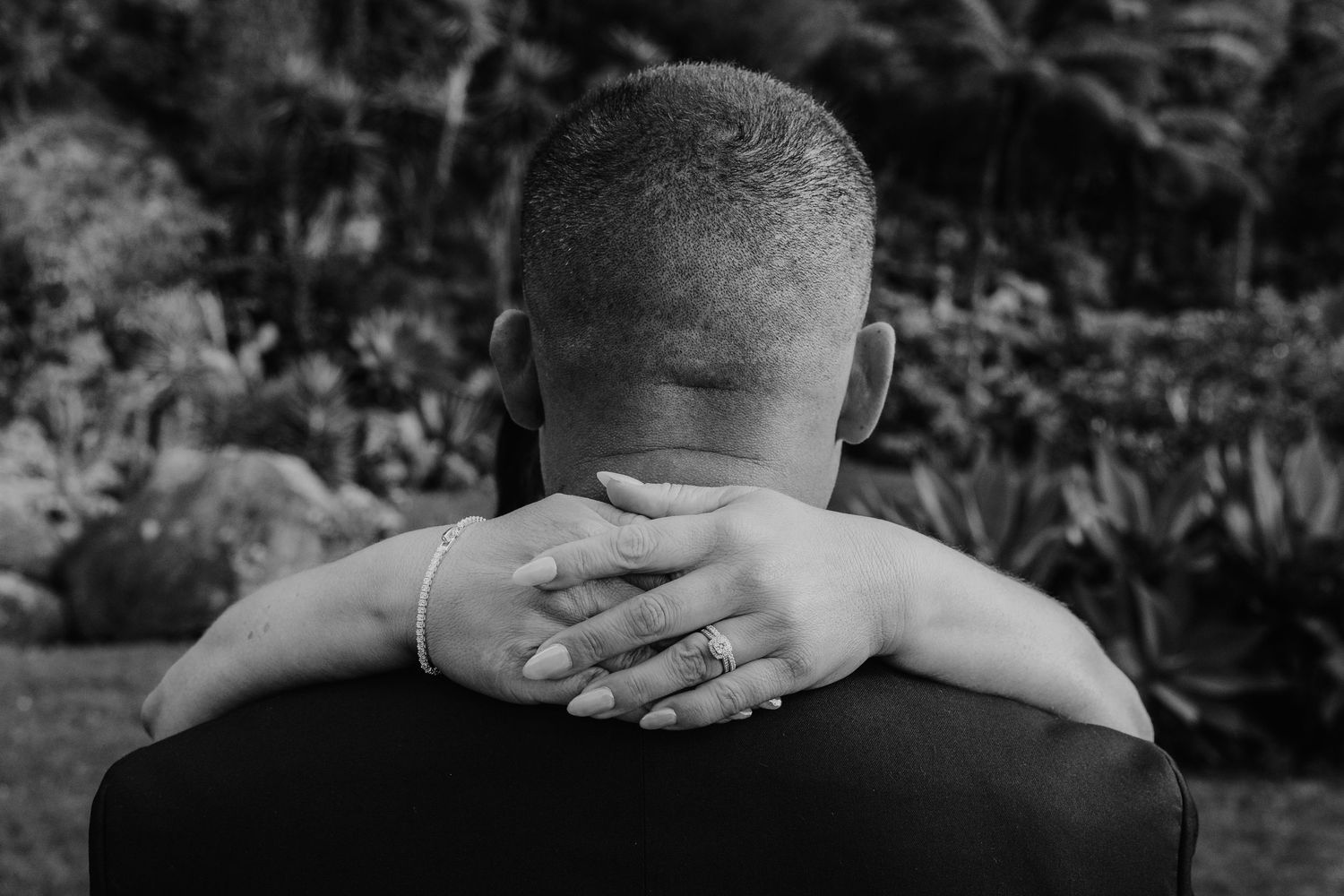 Black and white image of hands clasped behind a neck in a contemplative or relaxed pose outdoors.