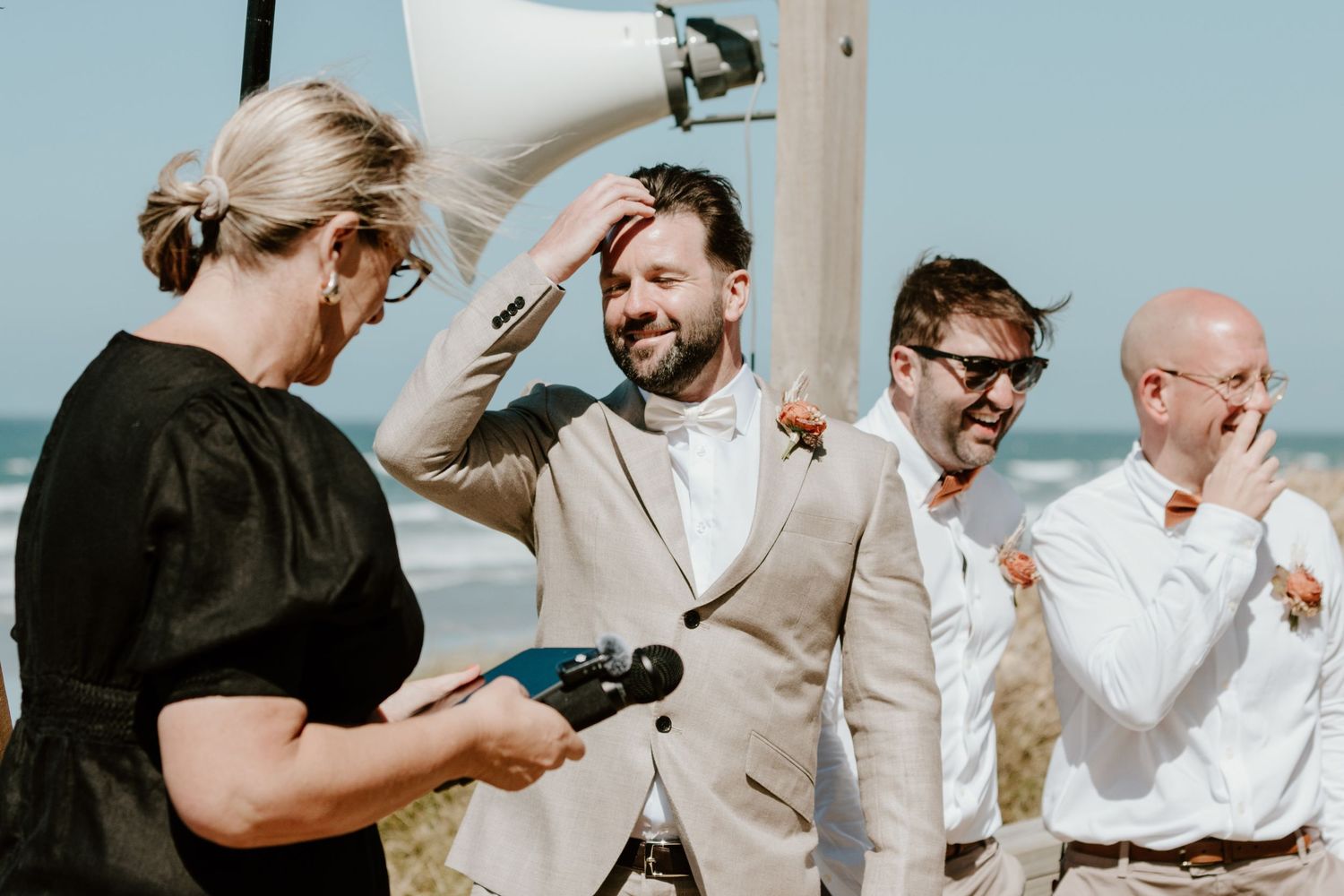 Wedding ceremony participants gather outdoors with celebrant speaking through a microphone. Papamoa Surf Lifesaving Club Wedding