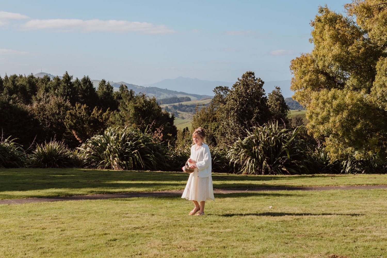 Wedding couple walks through lush gardens and rolling hills at a scenic outdoor venue on a sunny afternoon.