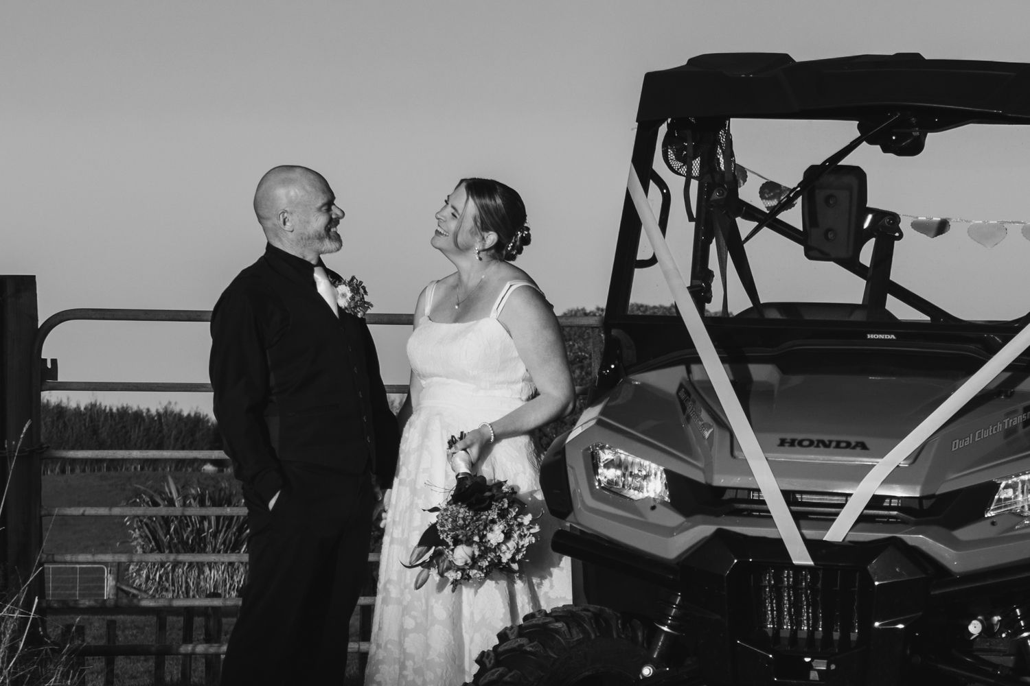 Black and white photo of a wedding couple sharing a moment next to a utility vehicle at an outdoor venue.