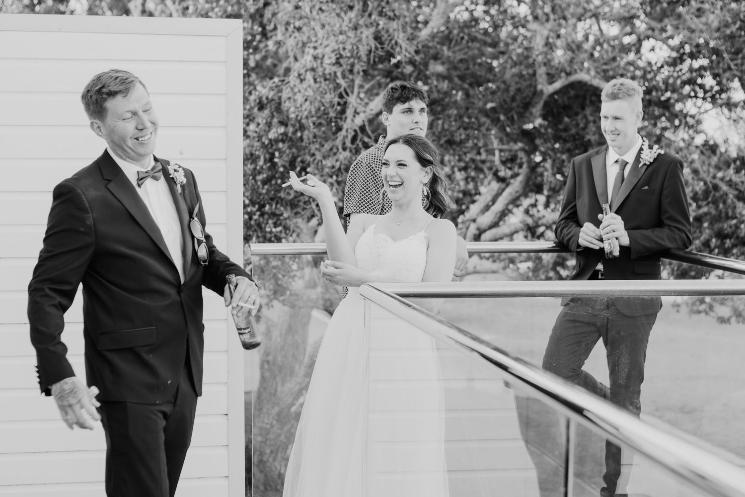 A candid black and white moment captured on a porch during a formal wedding celebration.