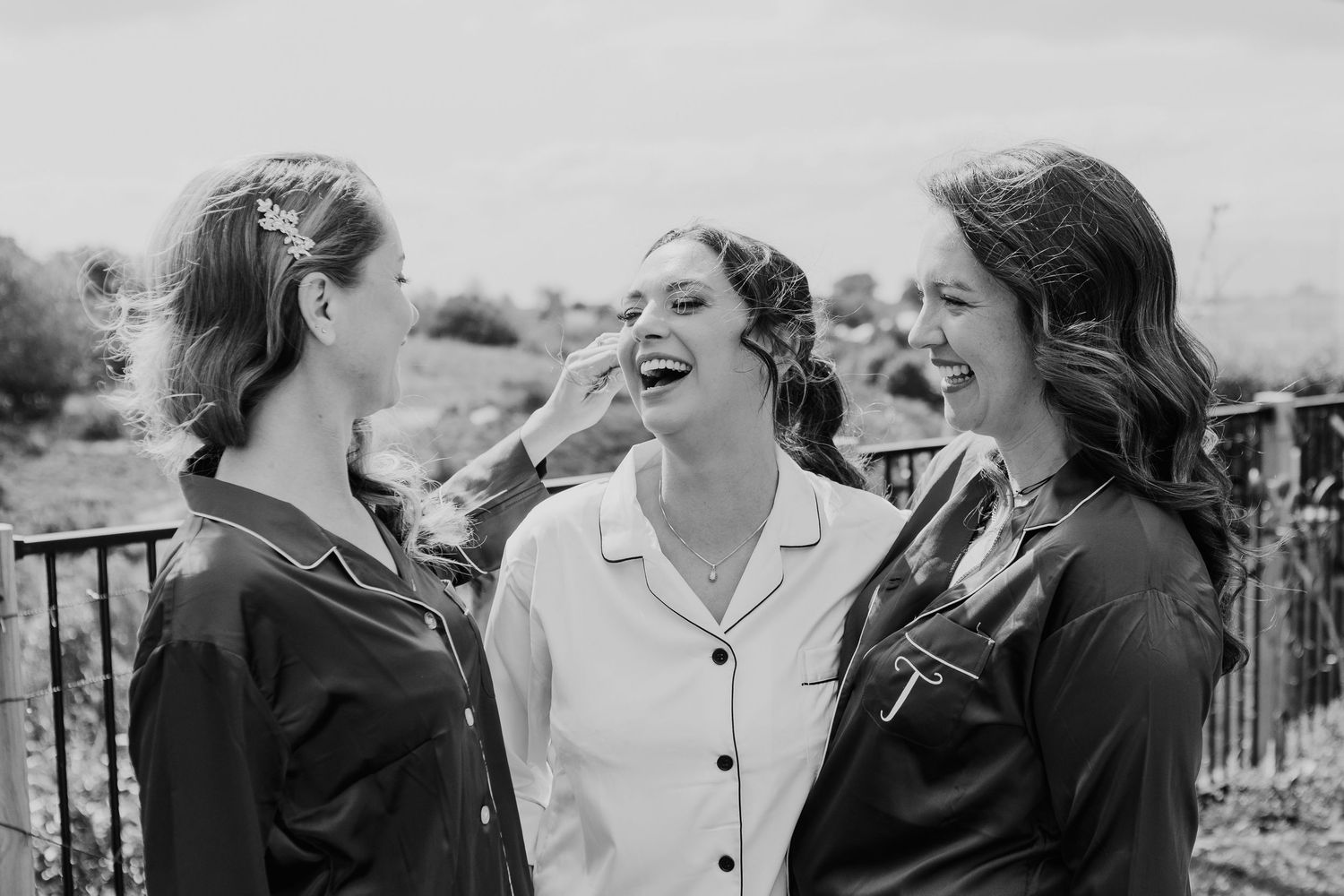Three people in black and white share a joyful moment of laughter together outdoors.