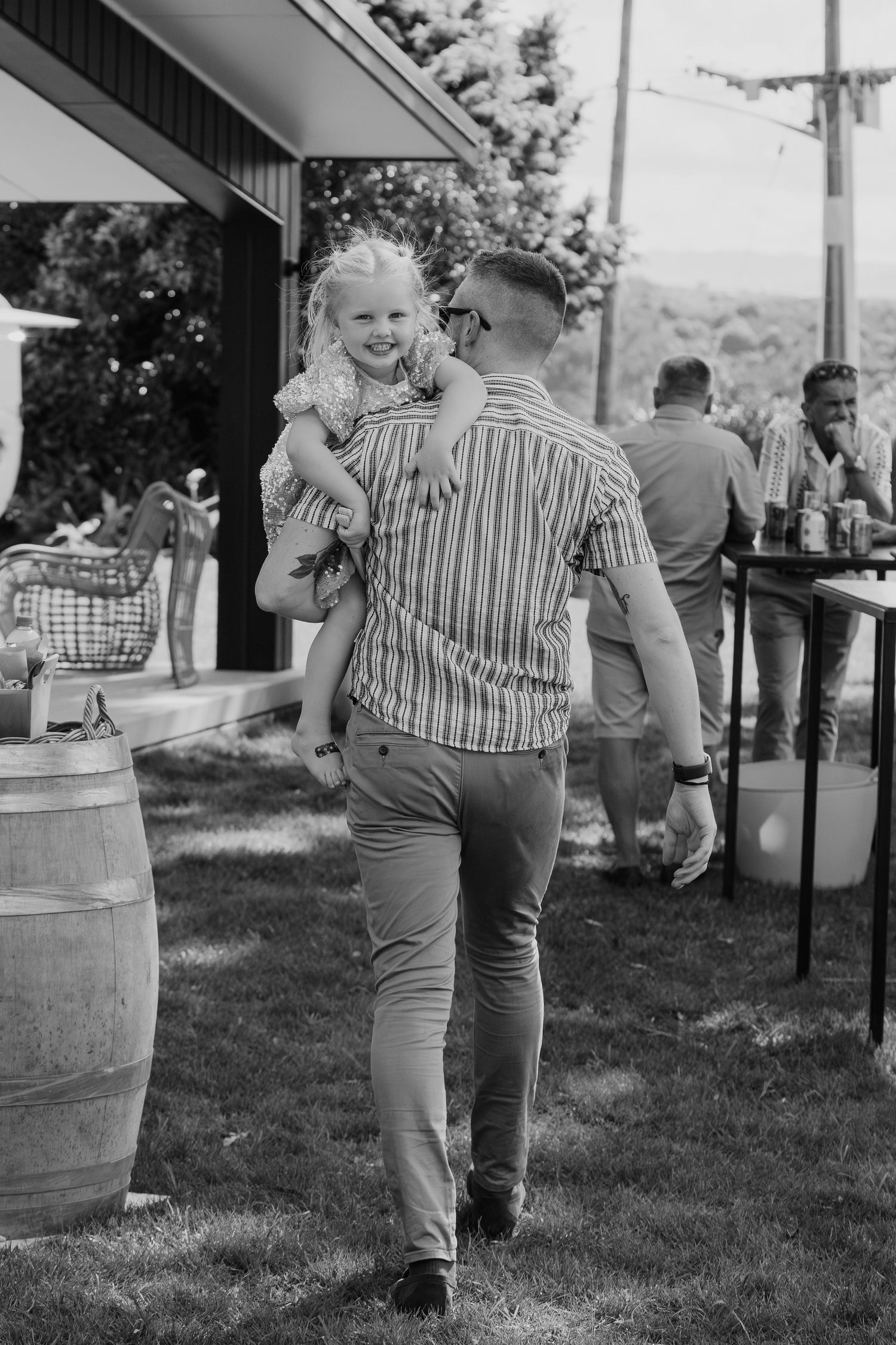 Black and white photo of a man carrying a smiling young girl at an outdoor garden party event.