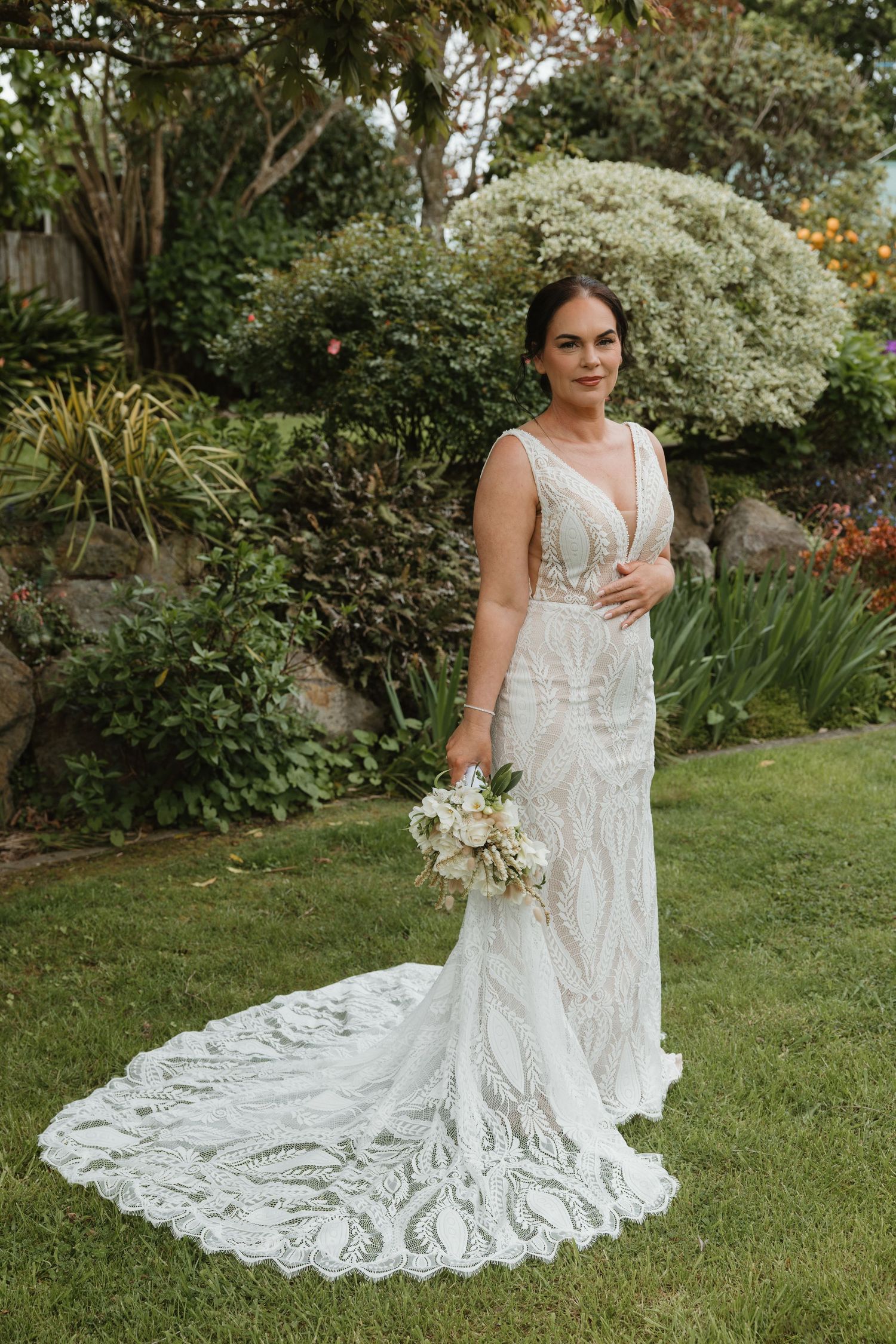 A bride in a vintage-inspired lace wedding gown with a dramatic train poses in a lush garden setting.