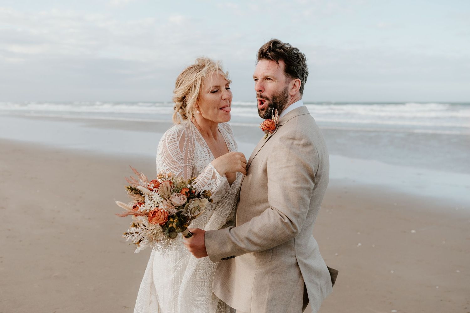 Wedding couple sharing intimate moment on sandy beach with floral bouquet. Papamoa Surf Lifesaving Club Wedding