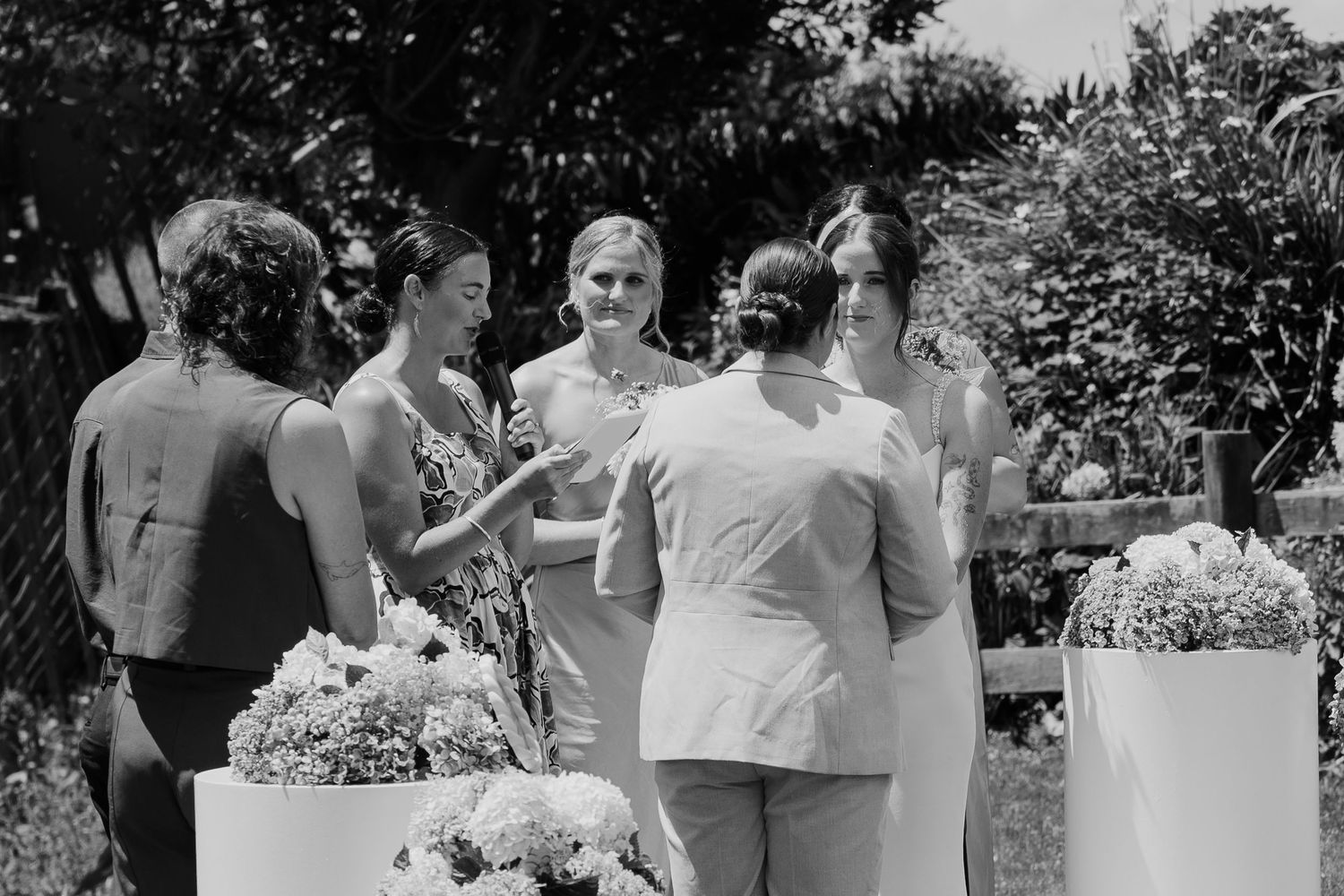 Black and white photo of women gathered outdoors at a garden event with floral arrangements.