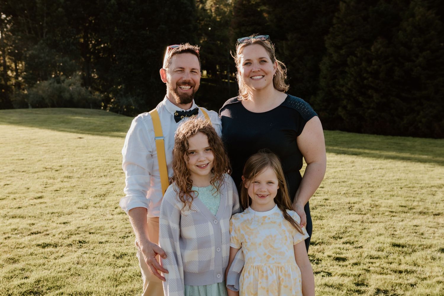 Three people pose together in a grassy meadow during golden hour, wearing coordinated blue and white outfits.