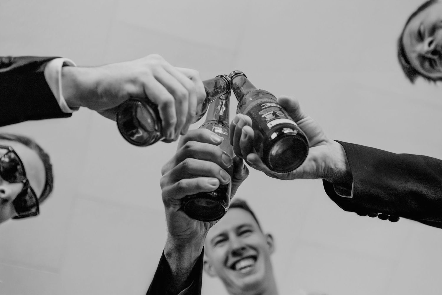 Multiple hands holding up drinks in a social setting make a celebratory toast together in black and white.