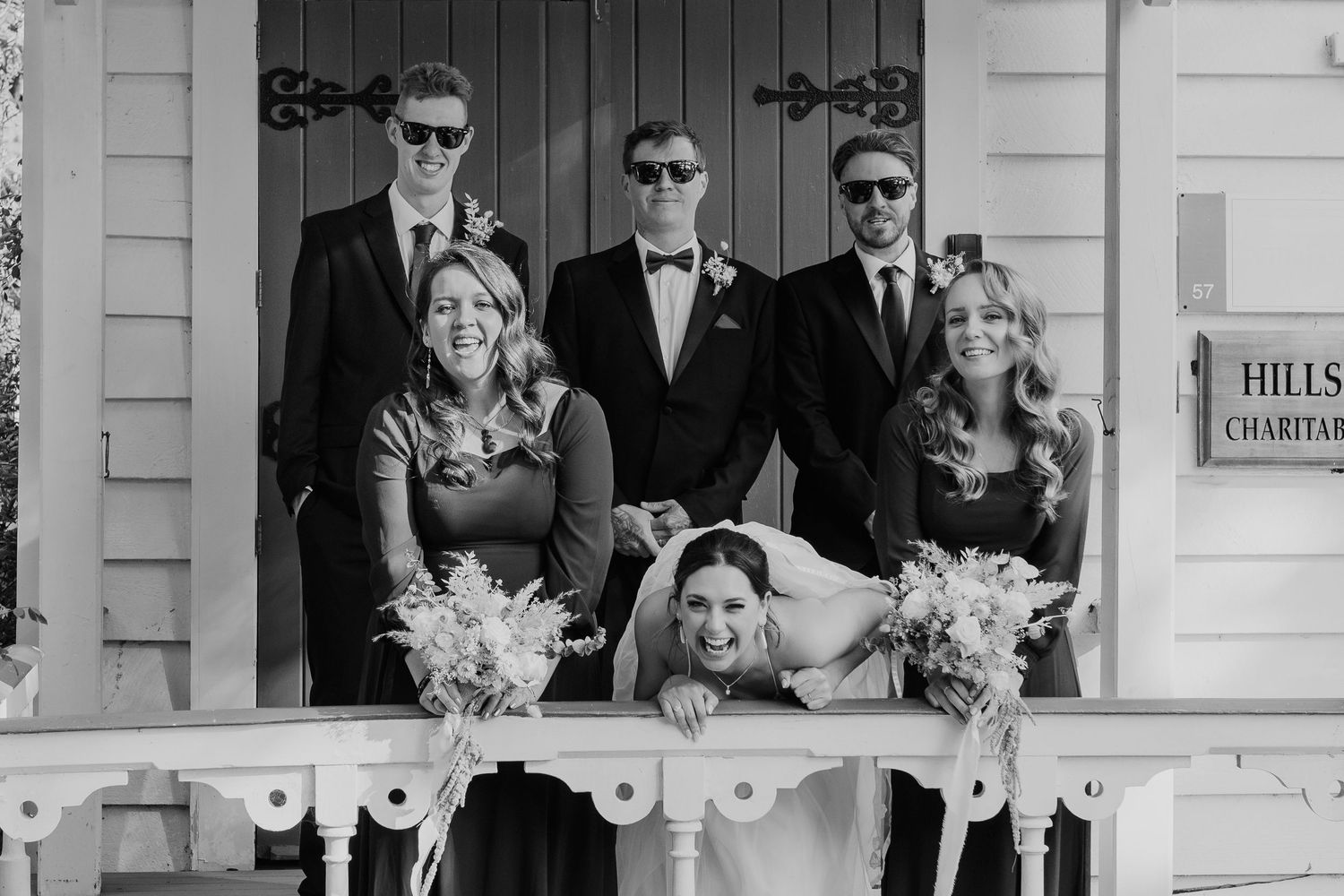 Black and white photo of a wedding party posing together on a porch with vintage architectural details.