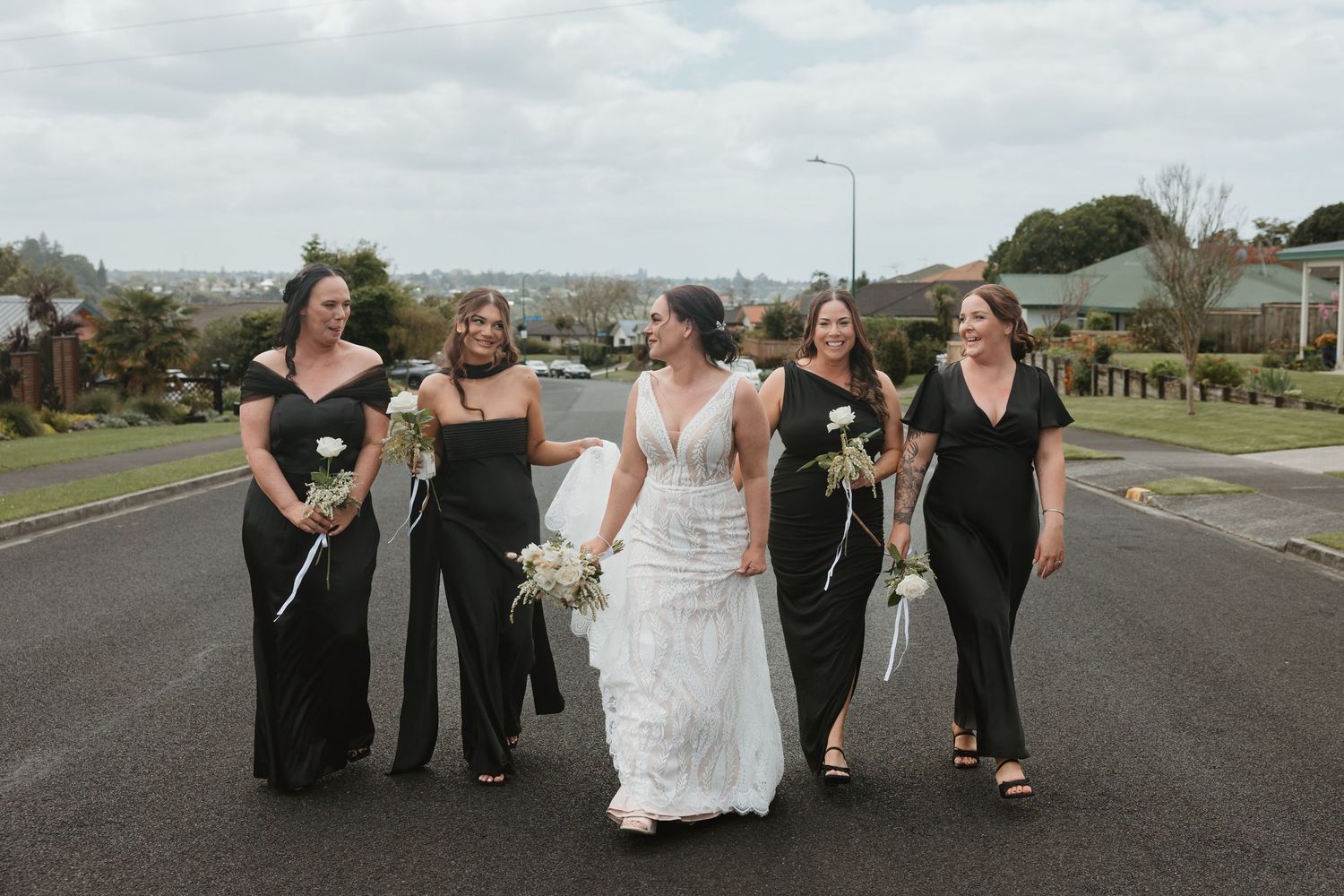 A group of people in formal attire walking and posing together on a road for wedding photos.