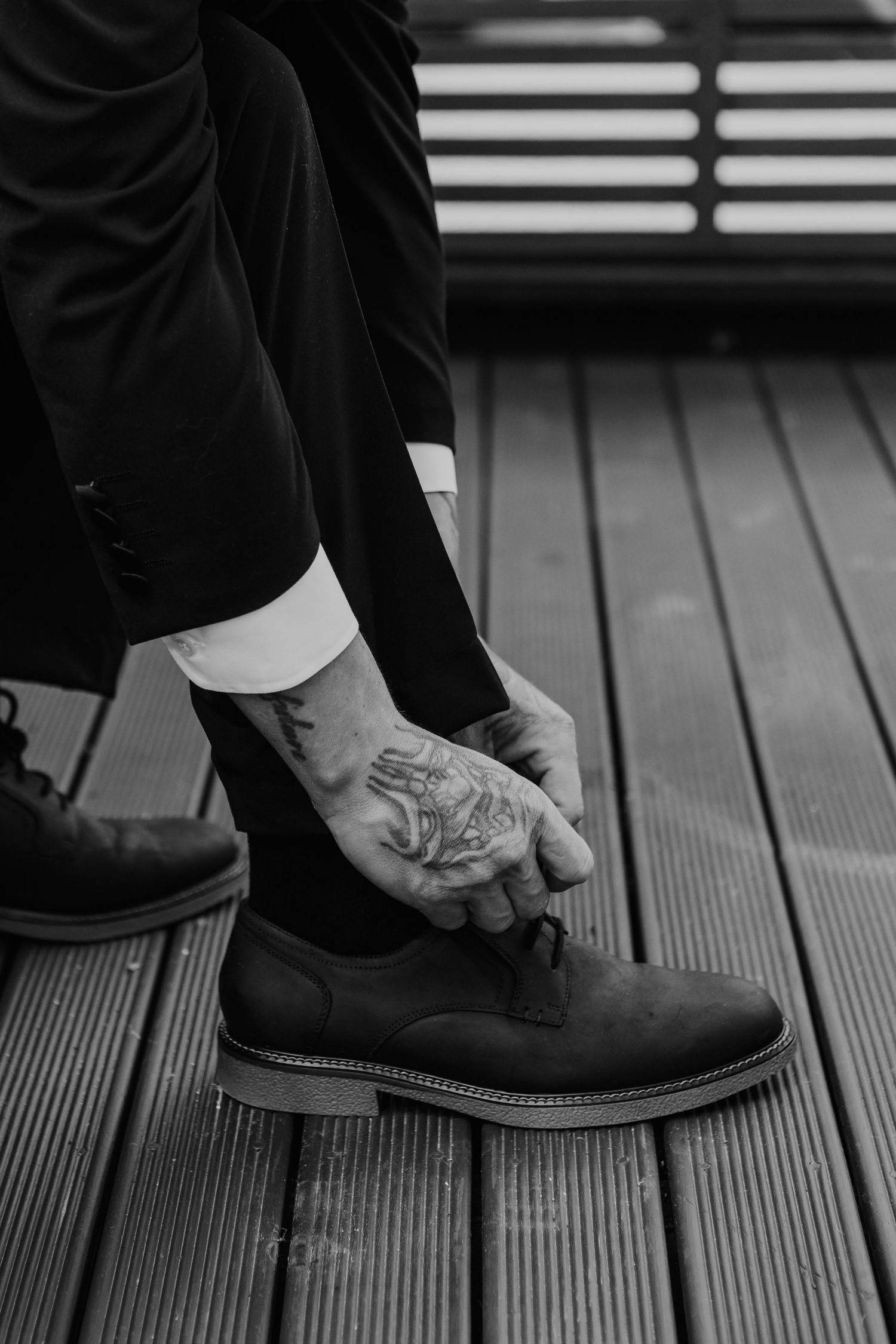 Black and white photo sequence showing someone putting on formal dress shoes on wooden deck planks.