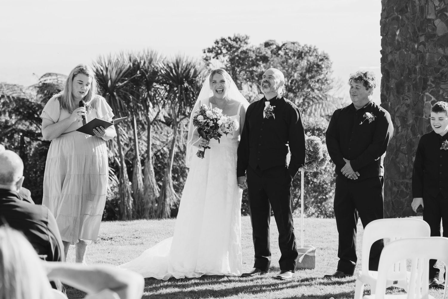A panoramic black and white wedding ceremony photo shows guests gathered outdoors under trees.