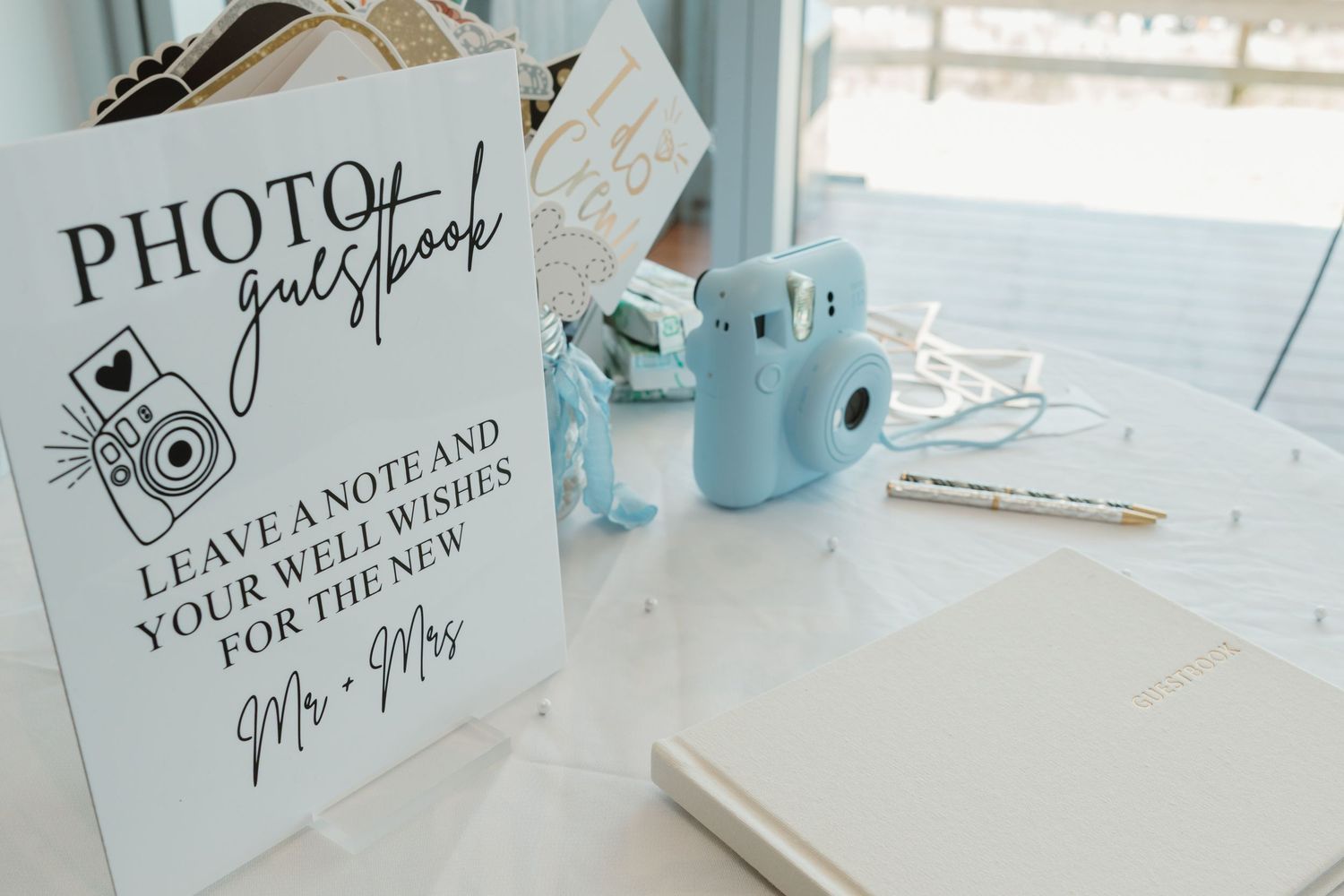 Photo guestbook sign with blue Instax camera and notebook on white table for wedding well wishes.