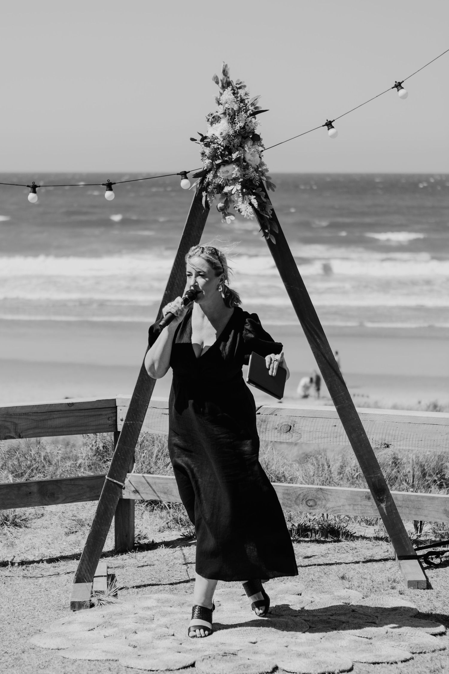 Black and white photo of wooden swing set on beach with string lights and ocean view. Papamoa Surf Lifesaving Club Wedding