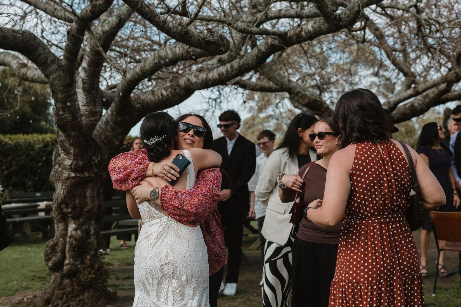 Guests dance and celebrate at an outdoor wedding reception under blooming cherry blossom trees.