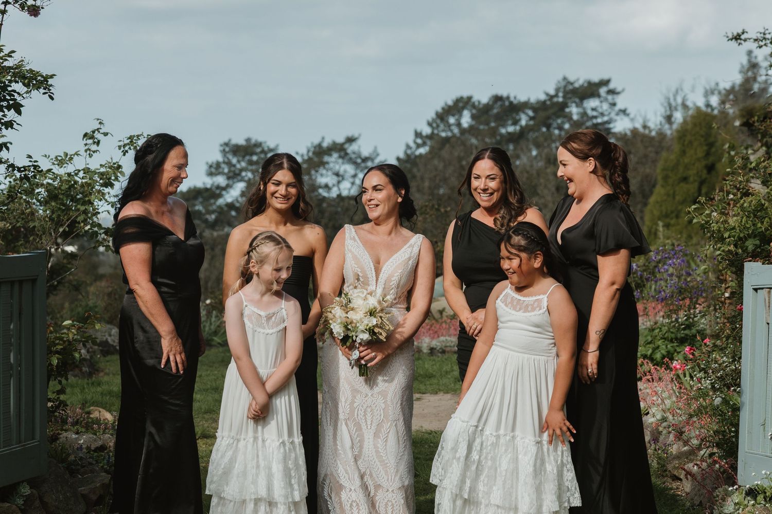 A group of bridesmaids in white dresses share laughter and candid moments during an outdoor wedding photoshoot.