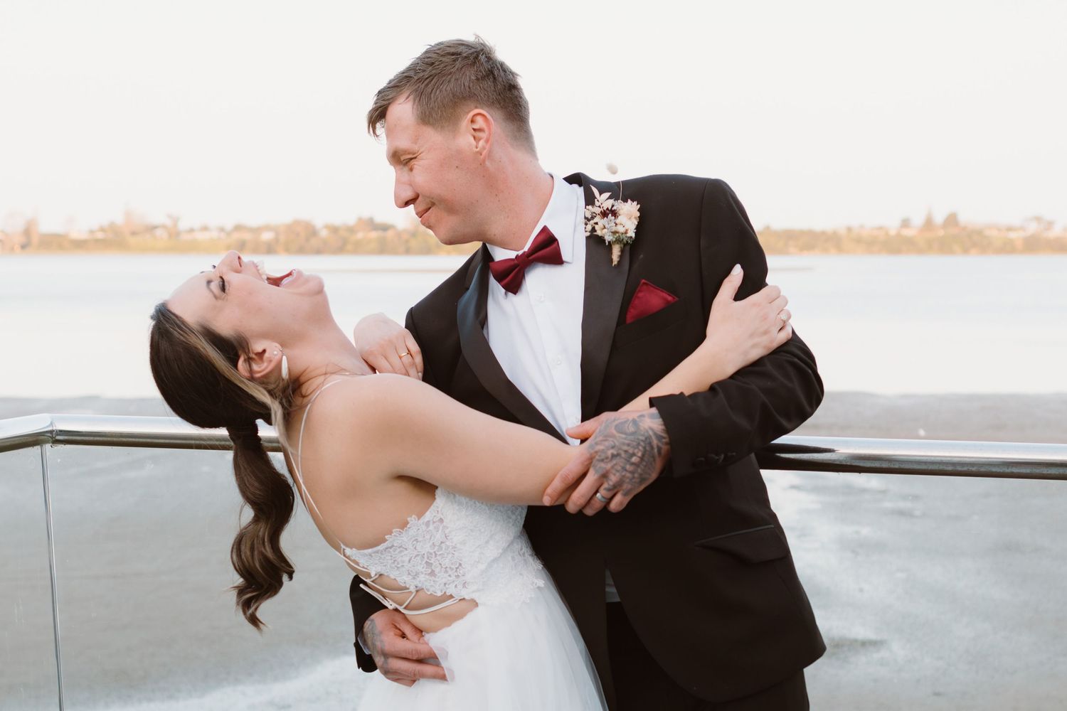 Romantic newlyweds share an intimate dance pose on a waterfront balcony at sunset.