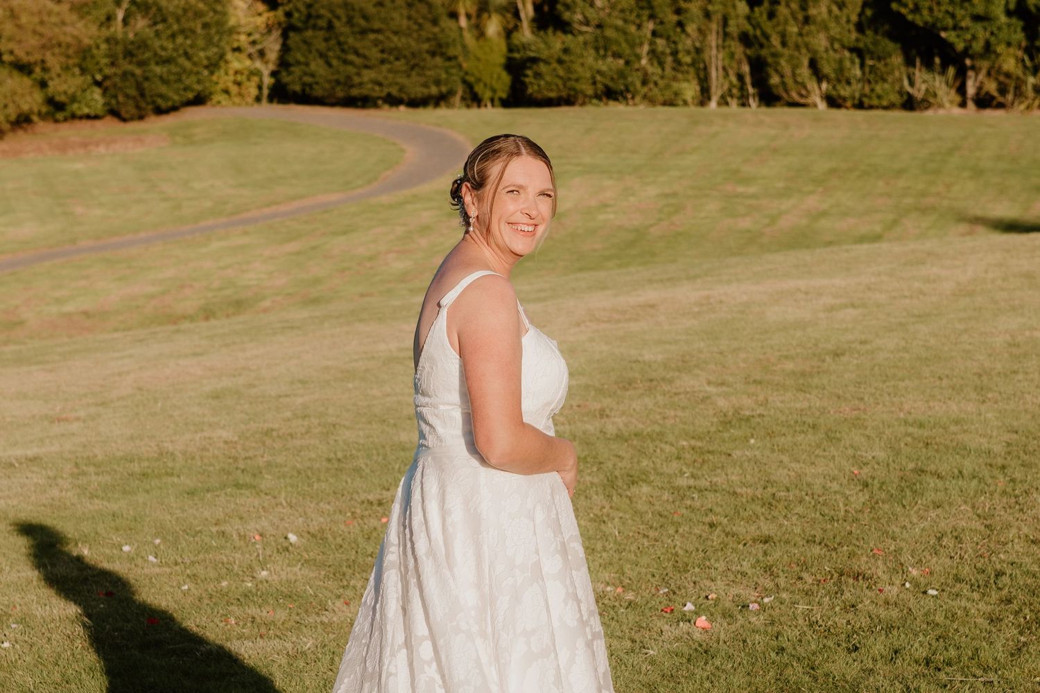 Someone wearing a sleeveless white lace dress stands in a sunny grassy field on a warm autumn day.