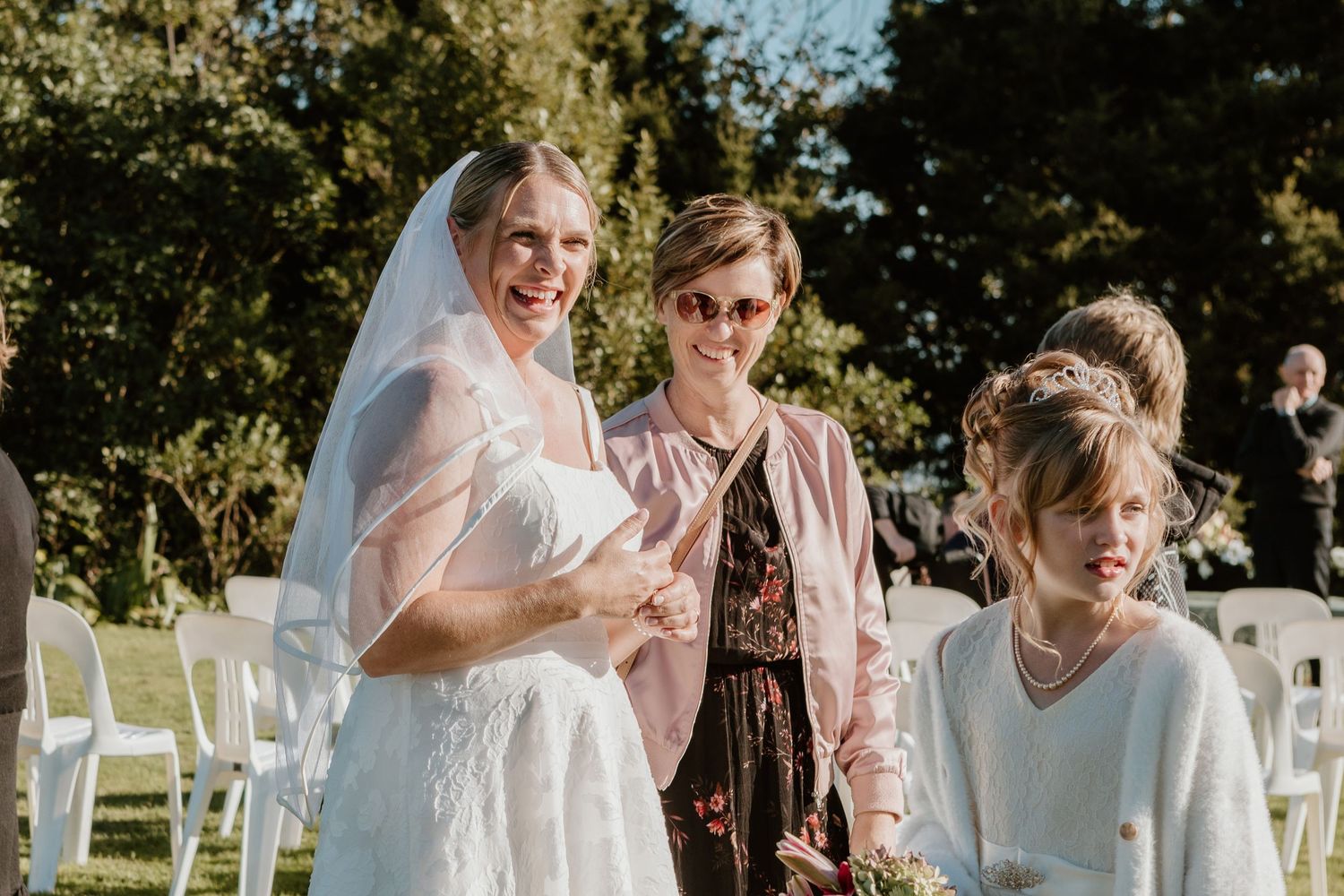 People celebrating at an outdoor wedding ceremony with white chairs on a sunny day.