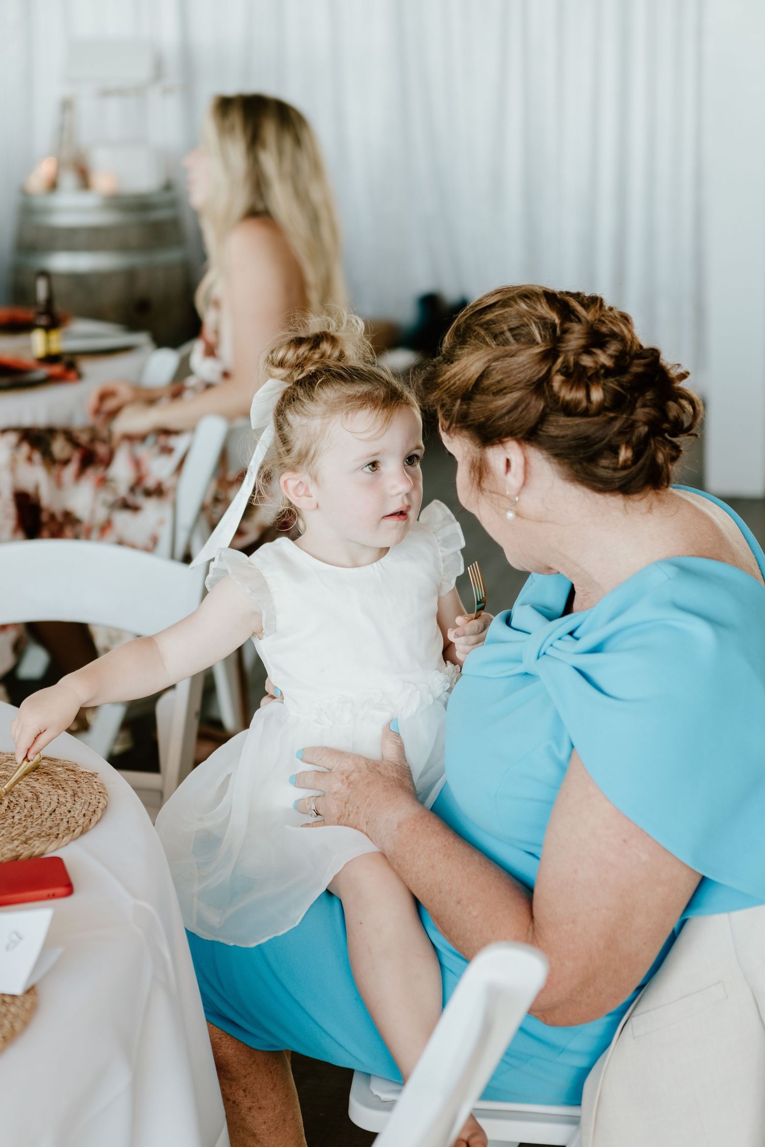 A sweet moment captured between an adult and child in white dress during a gathering, with soft natural lighting.