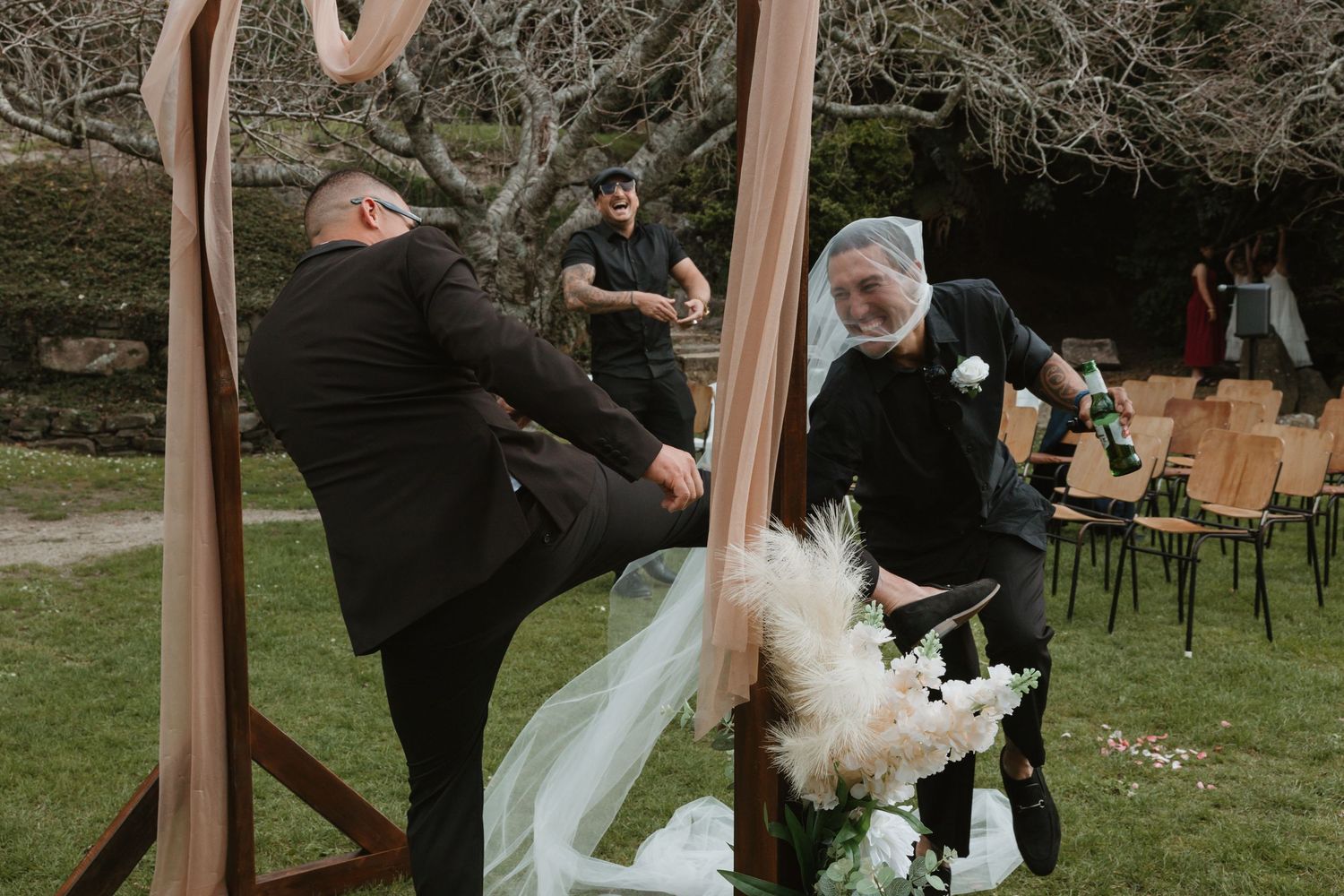 Newlyweds dance together at an outdoor garden wedding reception under wooden beams and string lights.