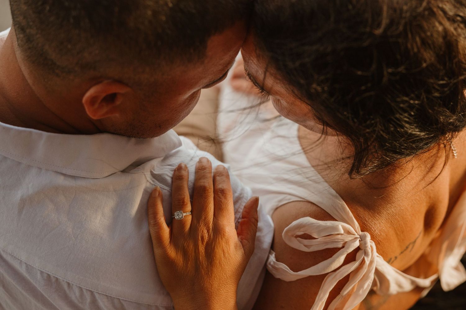 Intimate close-up shot of a couple embracing in warm sunlight wearing white clothing.