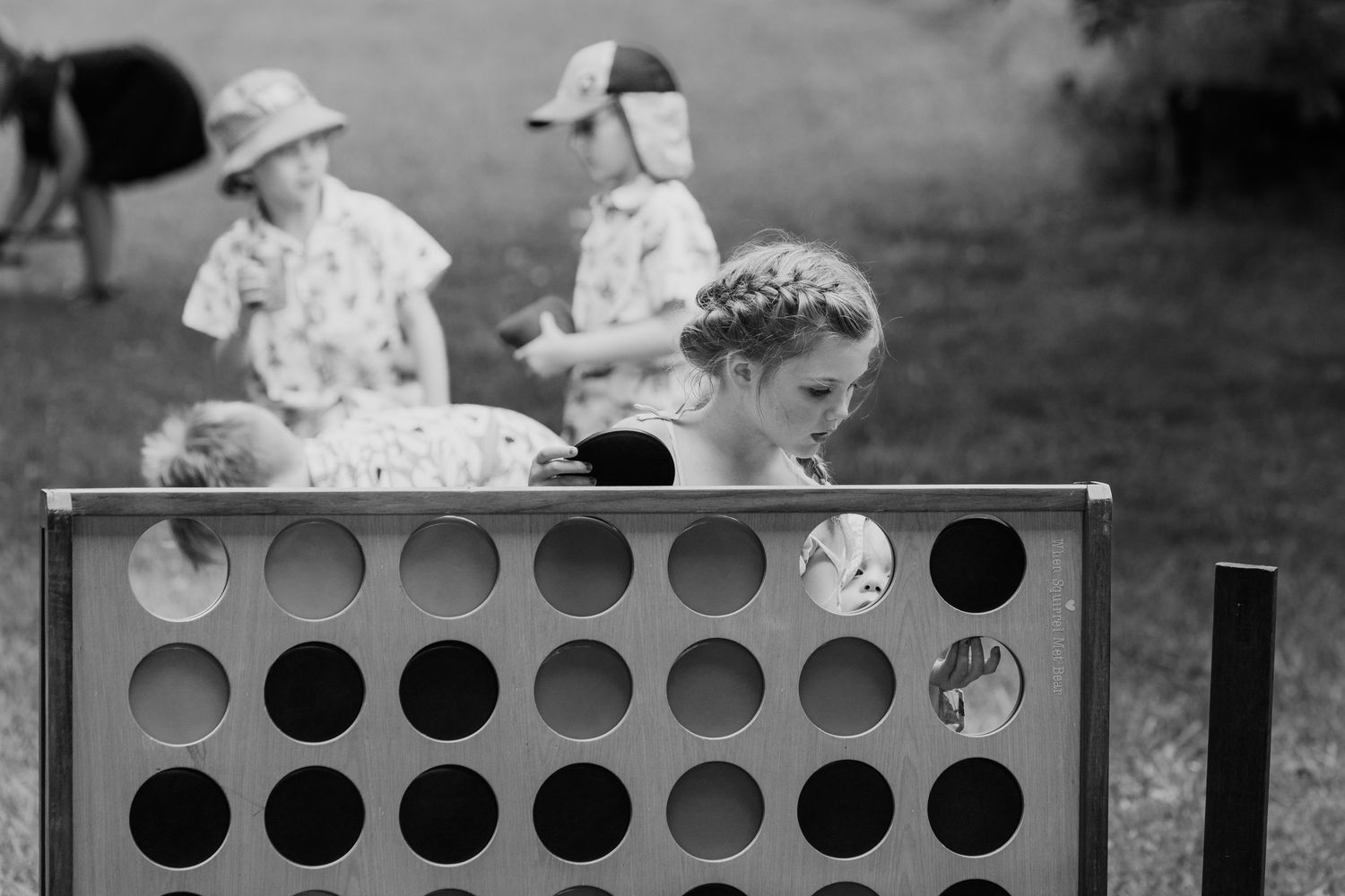 Children playing a giant Connect Four game outdoors in black and white photo.
