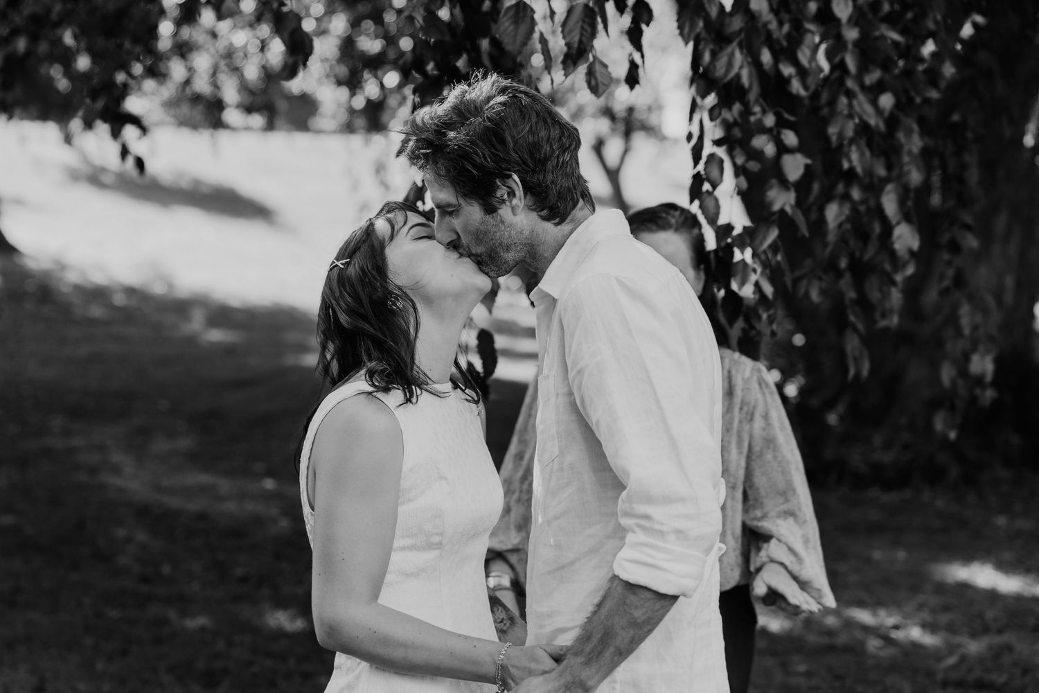 Black and white photo of a couple sharing a romantic kiss outdoors under a weeping tree at their wedding.