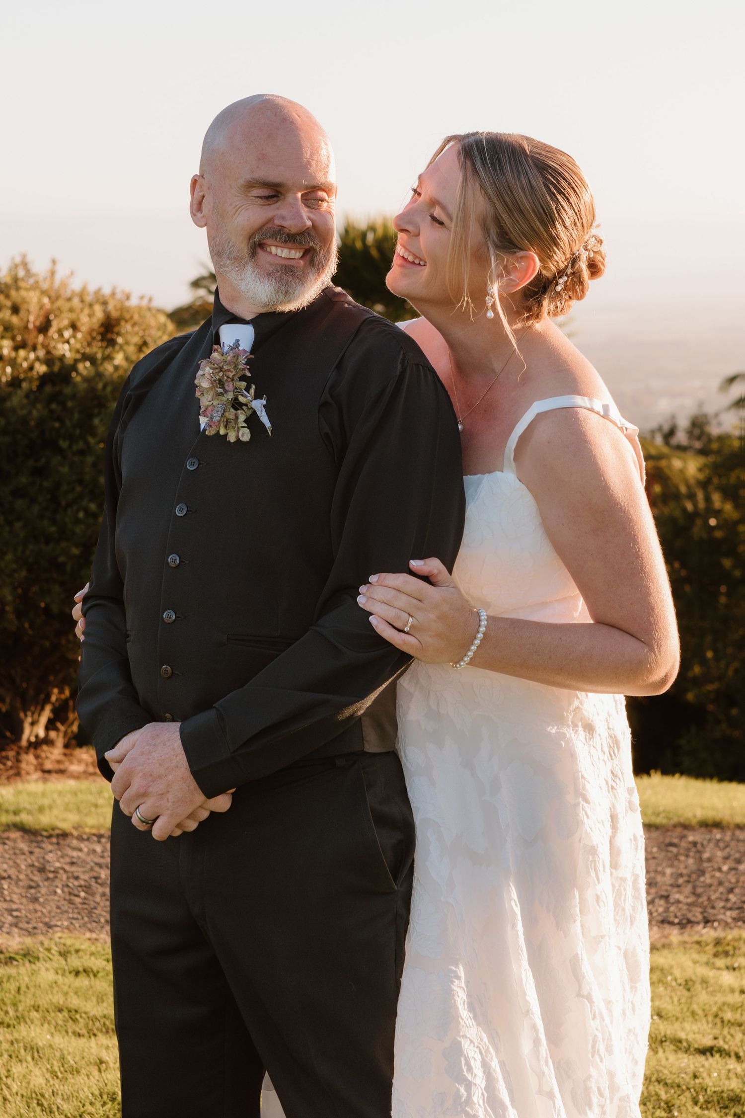 A bride and groom share joyful moments during sunset portraits at their outdoor wedding celebration.