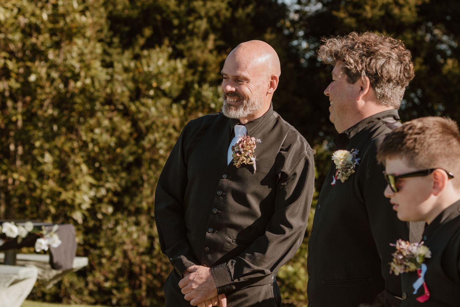 Wedding guests mingle and converse during an outdoor autumn ceremony with golden foliage in the background.