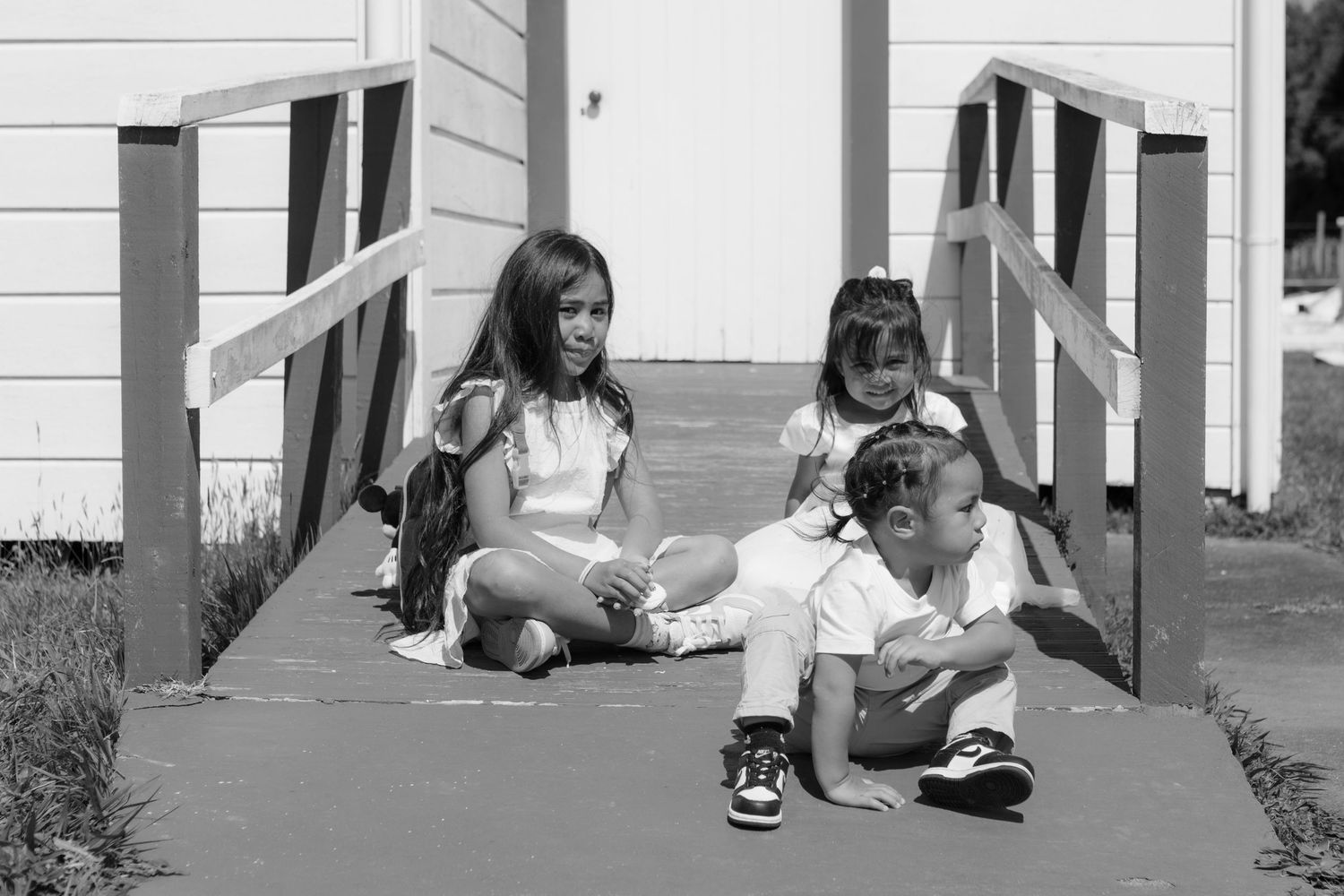 Three children sitting together on outdoor walkway steps in black and white vintage photograph.