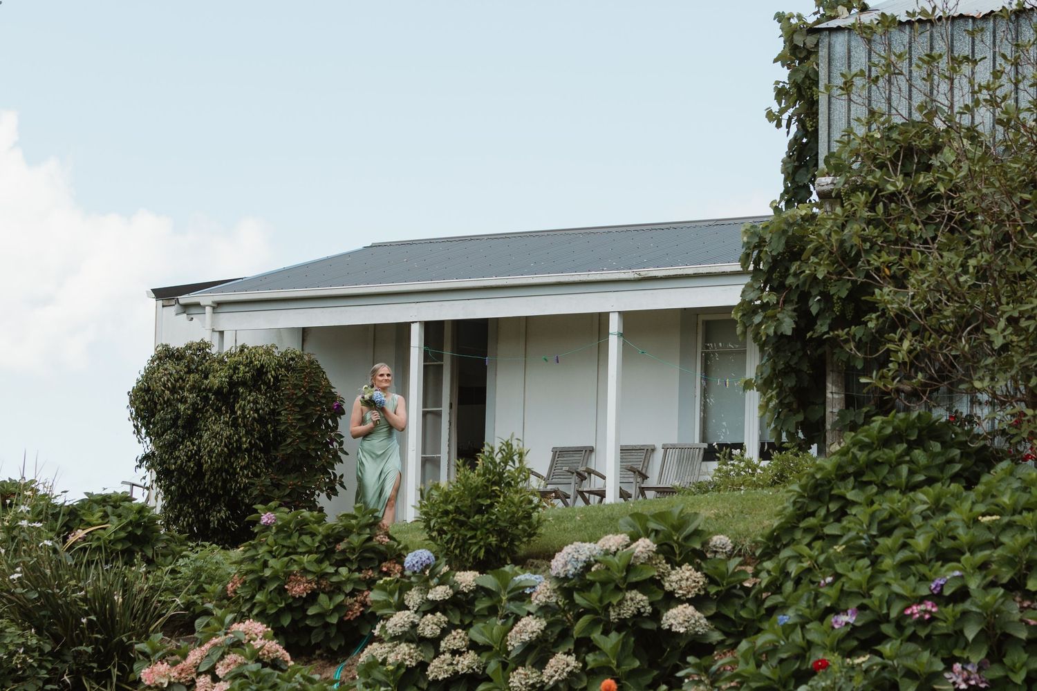 Woman standing on a veranda surrounded by lush hydrangea gardens at a charming country house.