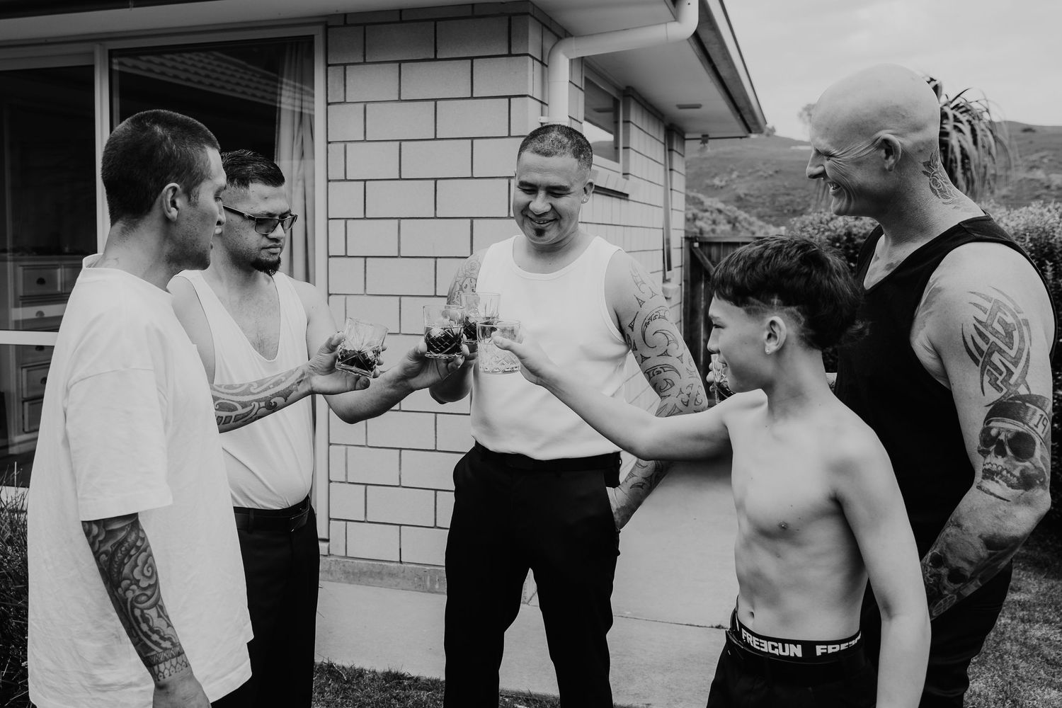 A black and white candid moment of people gathered outside a brick building, laughing and gesturing together.