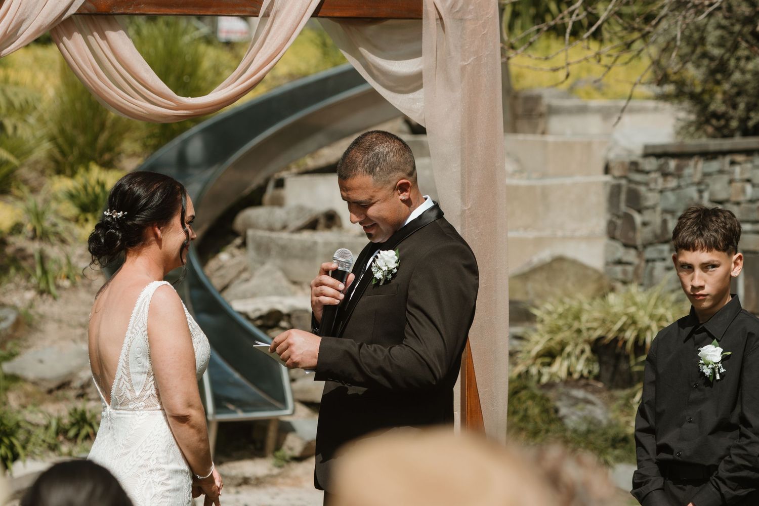 A couple shares an intimate moment during their outdoor wedding ceremony under a draped fabric canopy.