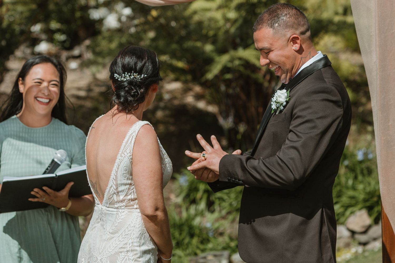 A joyful outdoor wedding ceremony with the couple and officiant sharing a lighthearted moment in natural sunlight.
