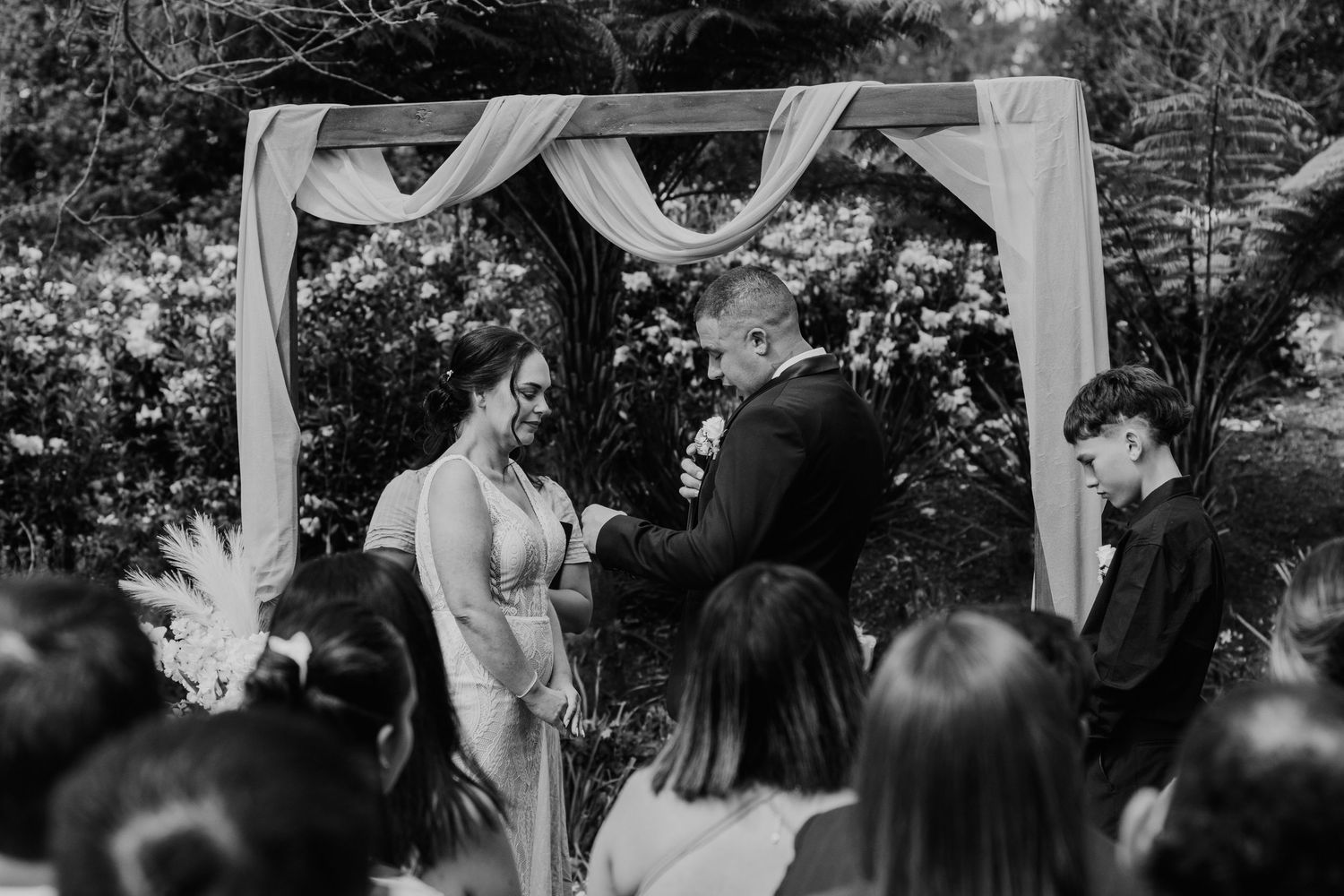 A romantic outdoor wedding ceremony under white fabric draping with guests seated in a garden setting.