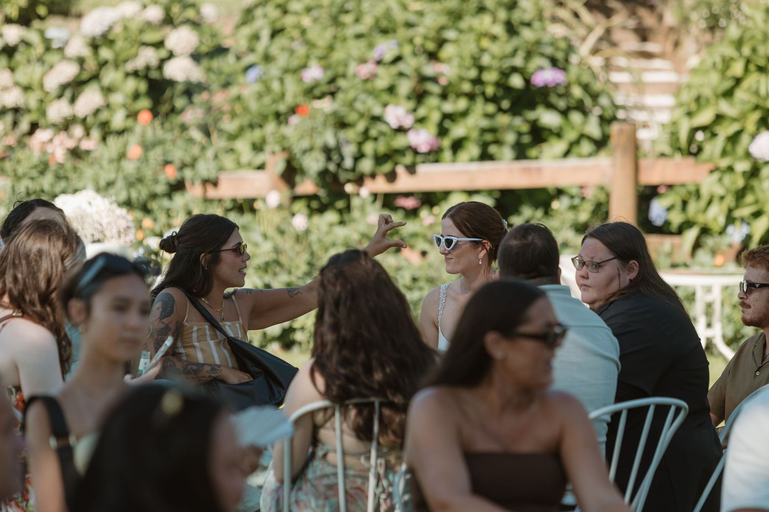 Guests socializing at an outdoor garden wedding reception, seated at tables surrounded by lush floral greenery.
