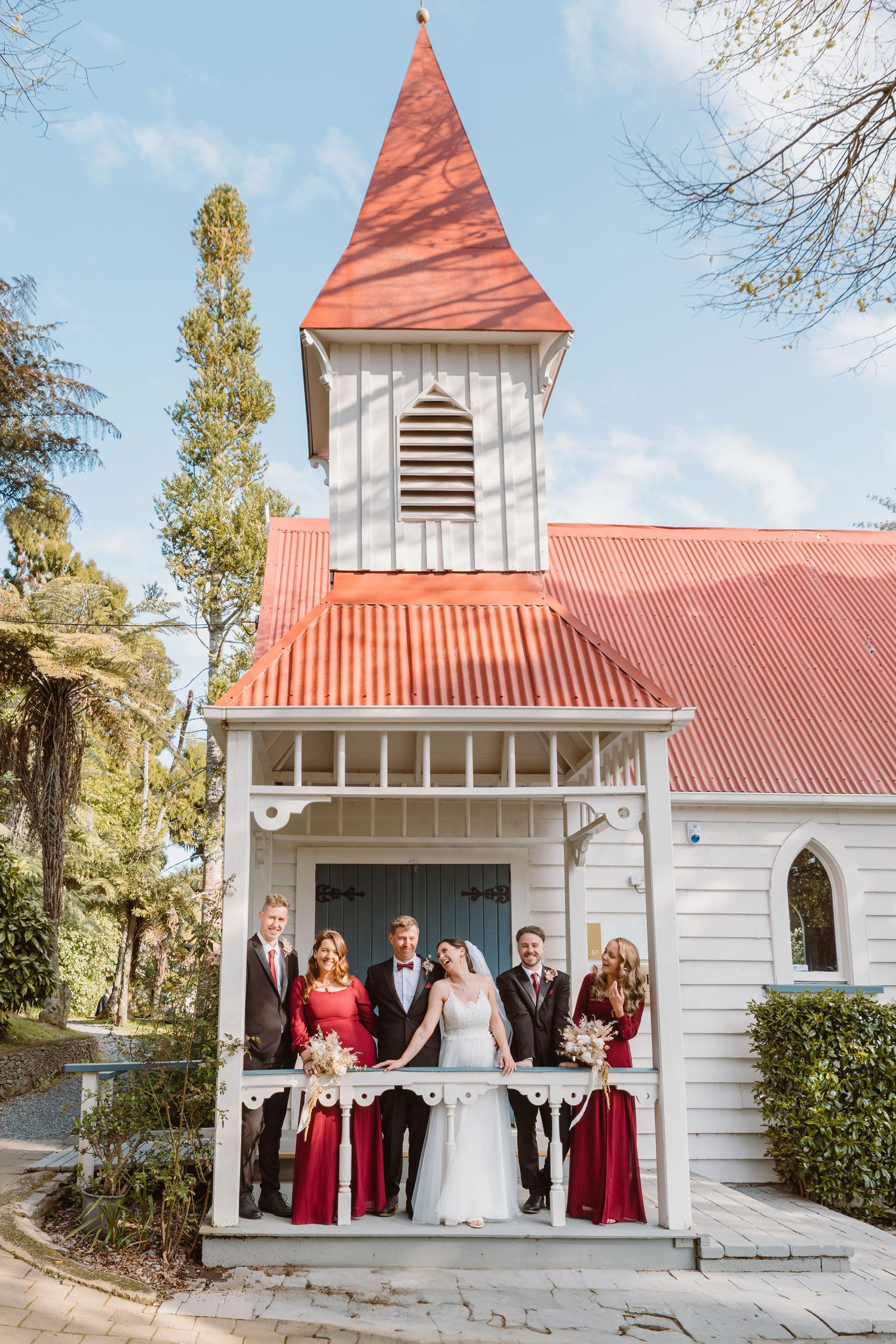 Charming white chapel with red roof and spire features a covered porch entrance on a sunny day.