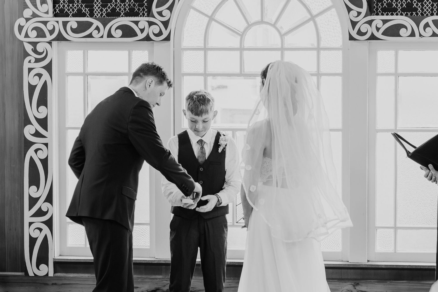 A black and white photograph capturing a tender wedding ceremony moment in an elegant church setting.
