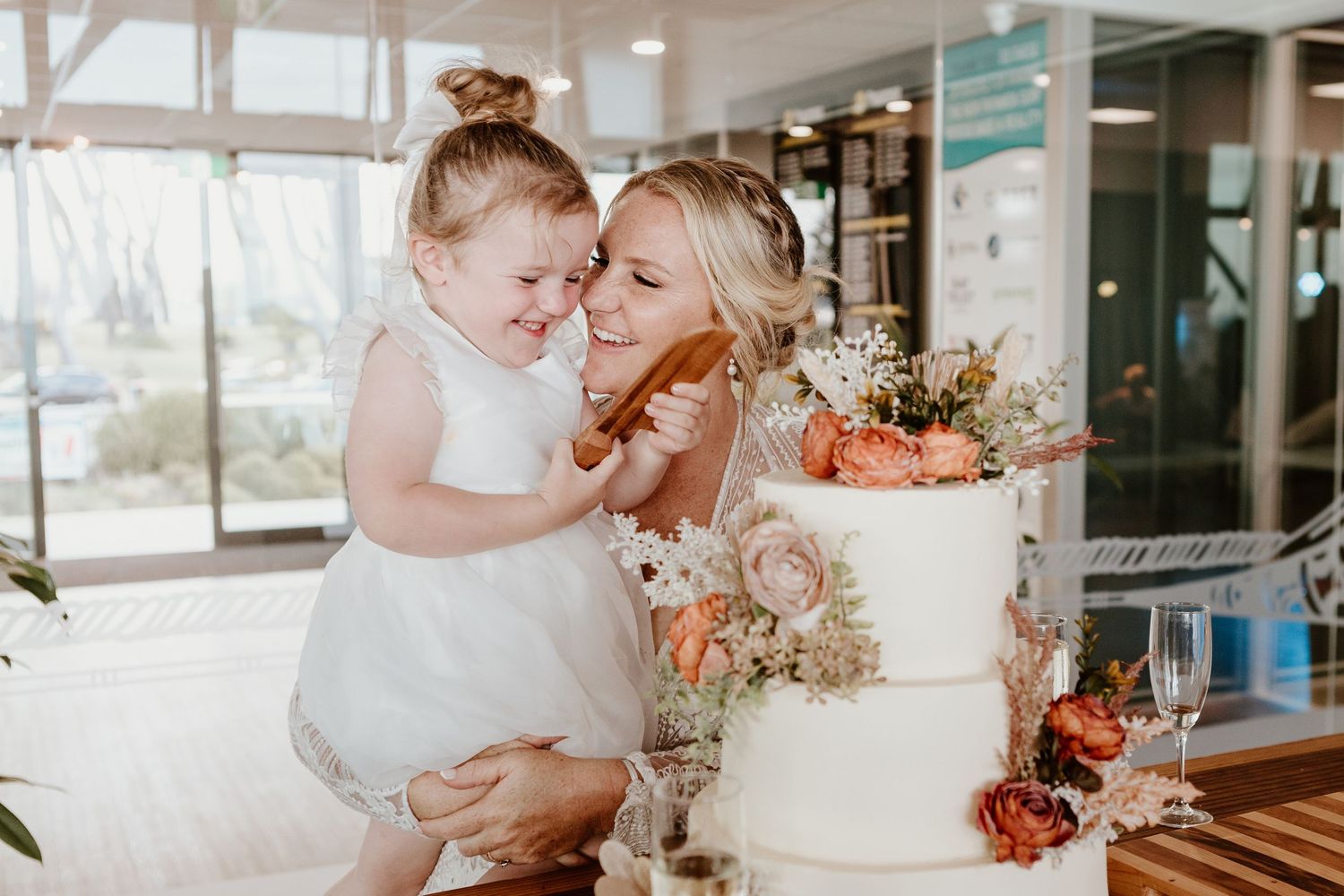 Two people embrace in a tender moment during a wedding ceremony with peach floral decorations in the background.