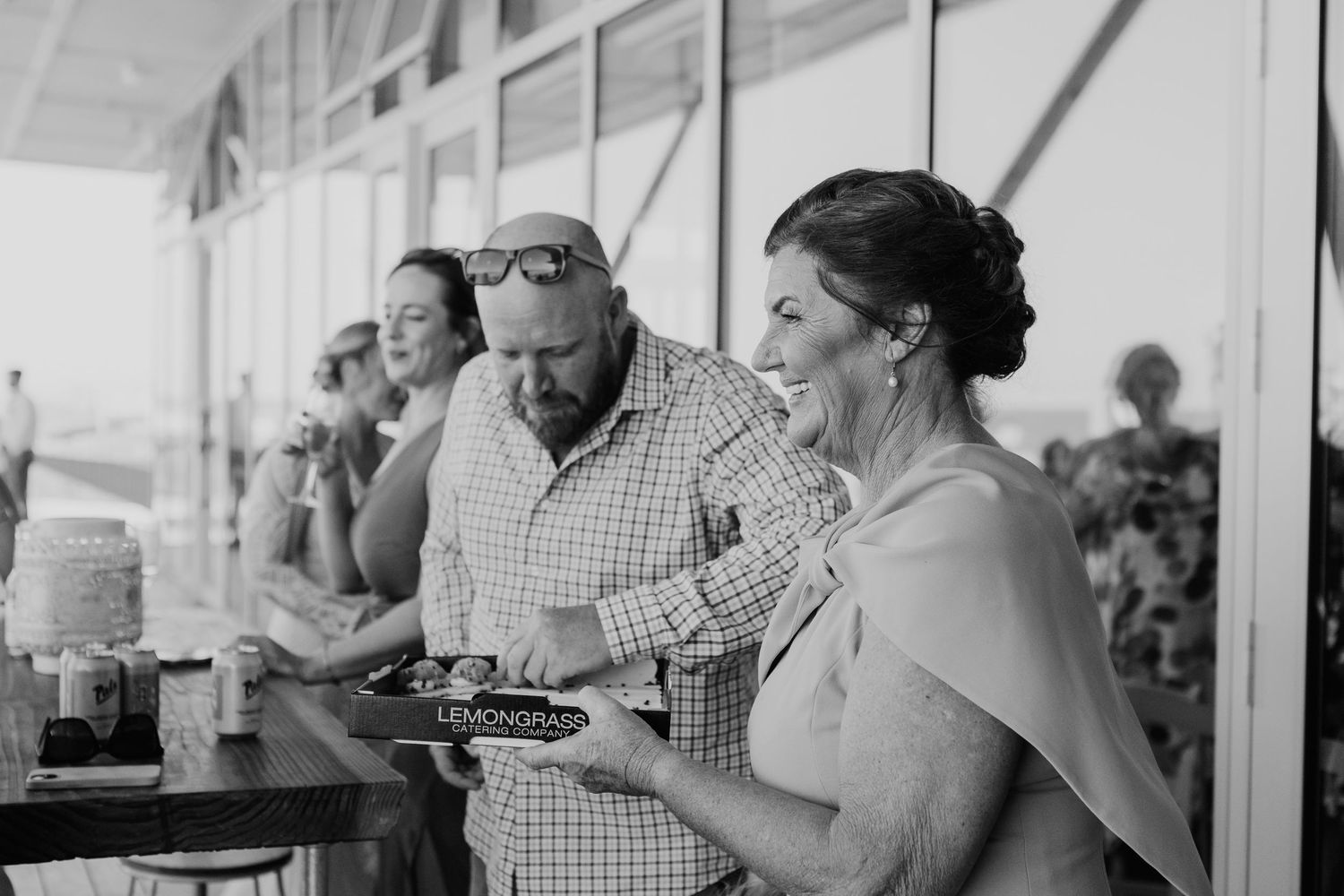 A black and white photo of people laughing and enjoying food at an outdoor gathering.